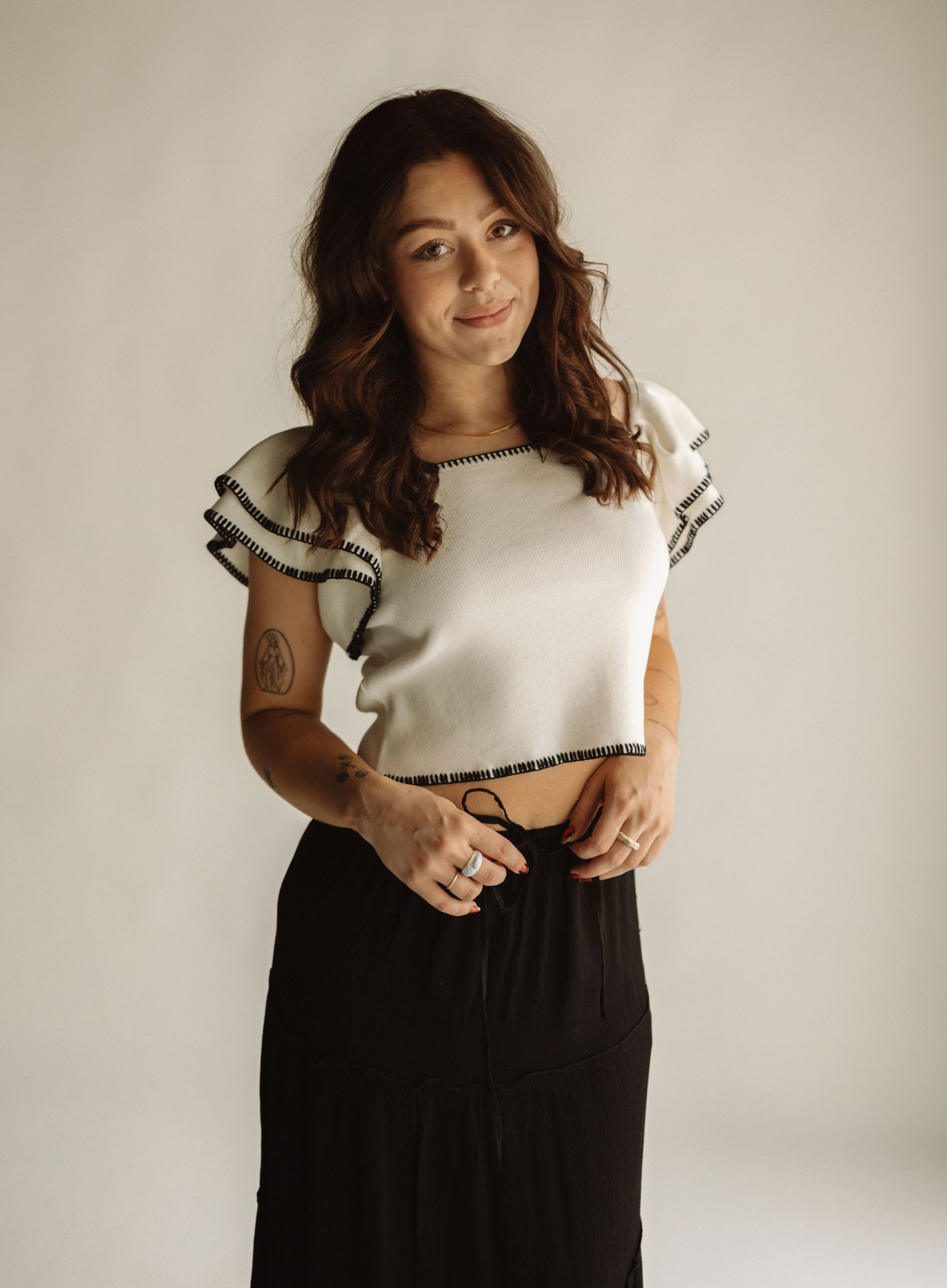 Woman in white sleeveless top and black high-waisted pants posing in four different angles against neutral background.