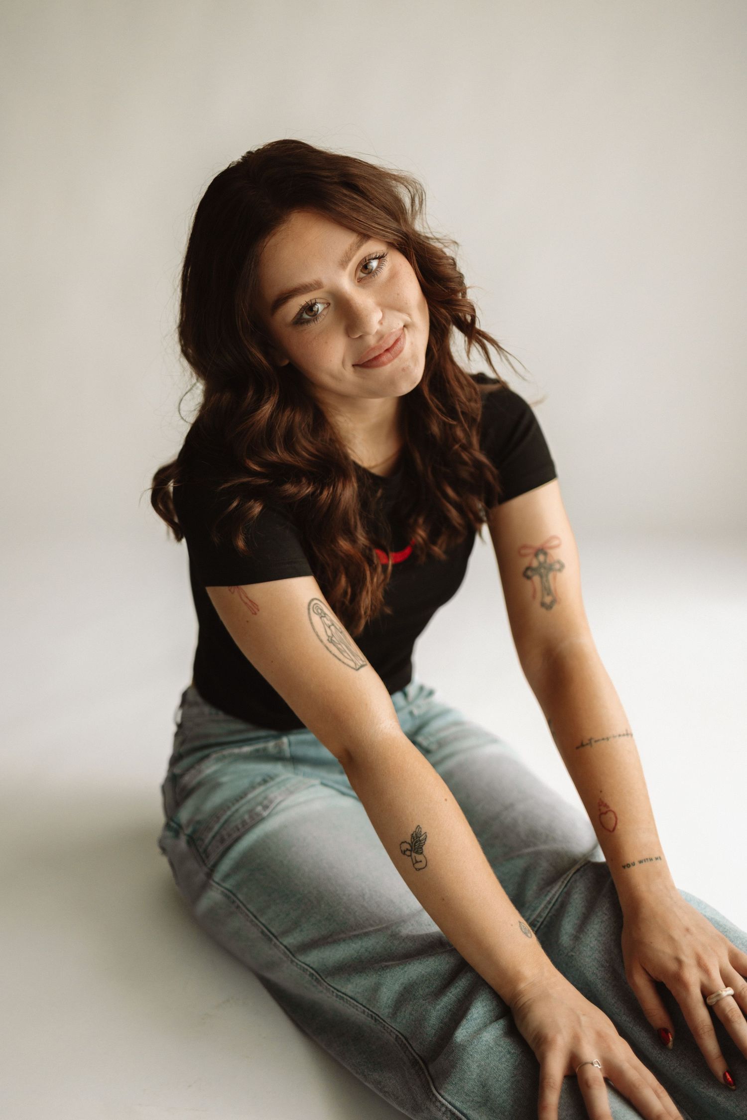 Model in black t-shirt and light jeans poses on white background while sitting and leaning in different positions.