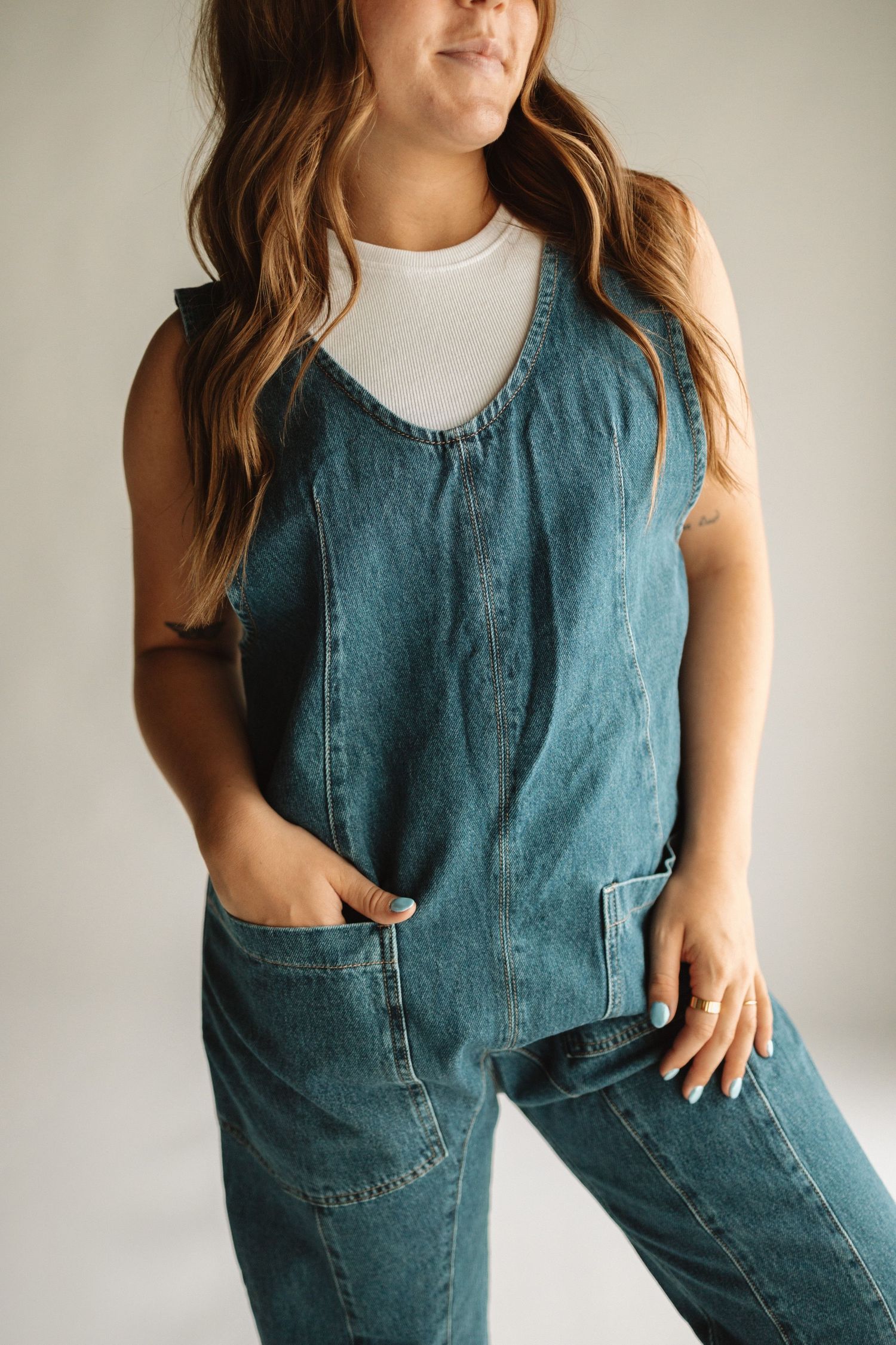 A casual denim jumpsuit paired with a white sleeveless tank top creates a relaxed, modern look.