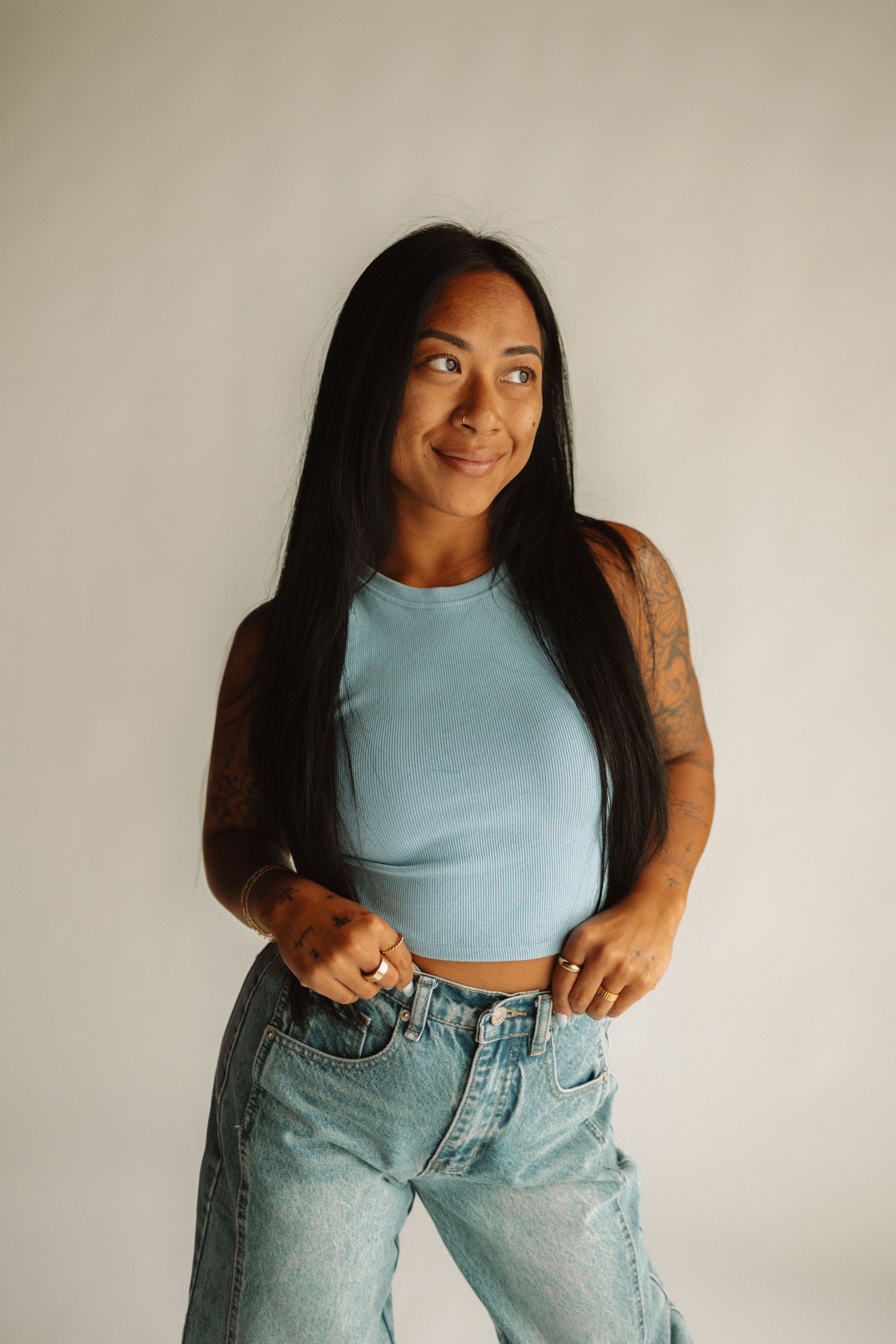 Person in light blue crop top and loose-fitting jeans poses playfully against white background in fashion lookbook series.