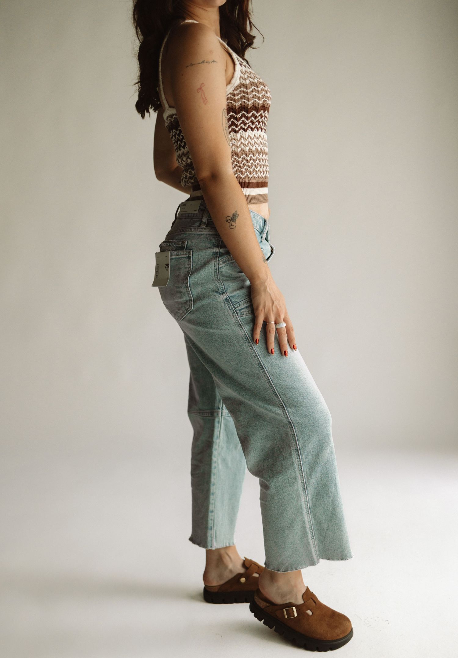 Side view of someone wearing a patterned knit tank top with light wash cropped jeans and brown buckled shoes.