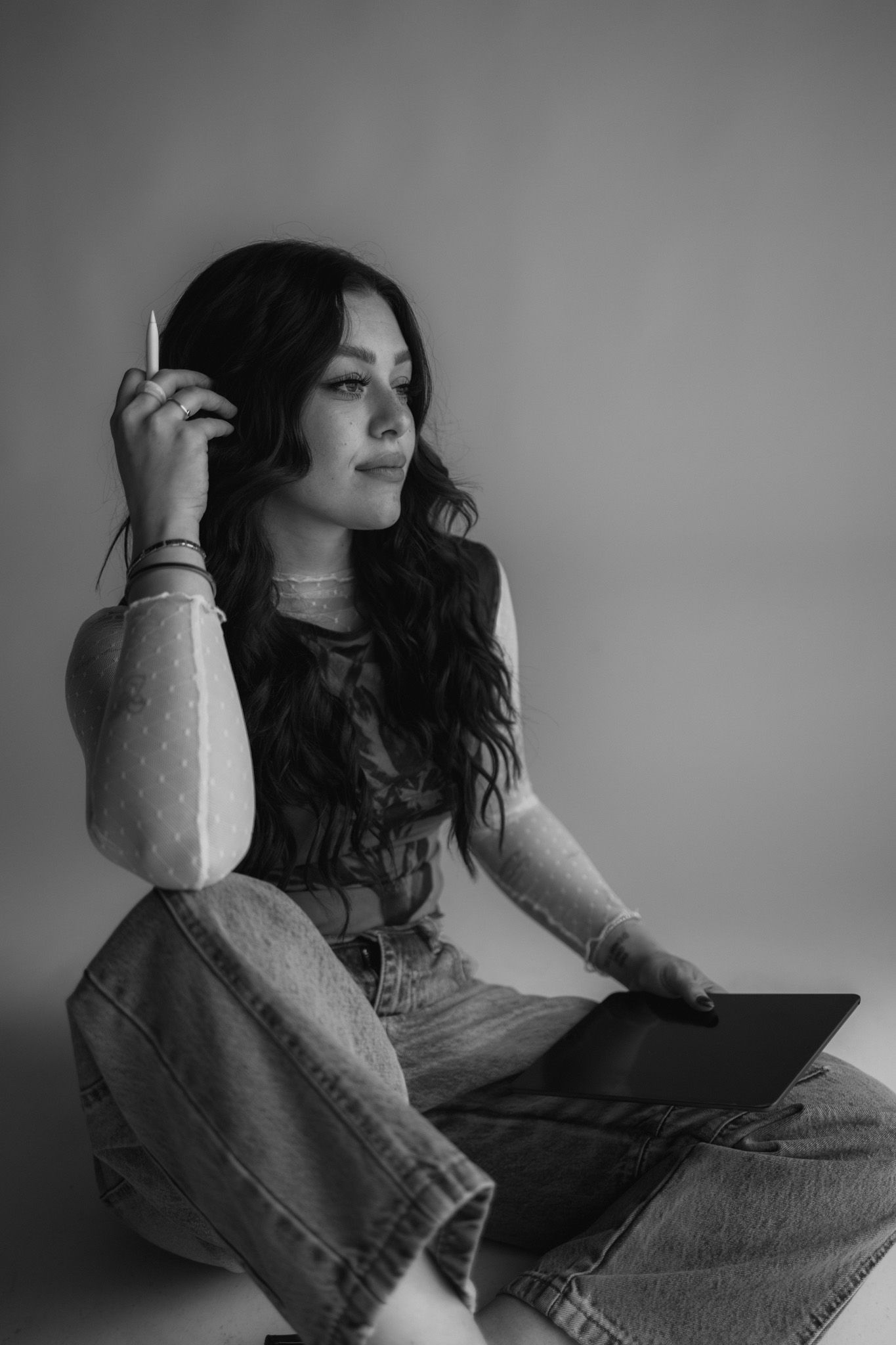 Black and white portrait of a person in casual denim looking contemplative while sitting against a wall.