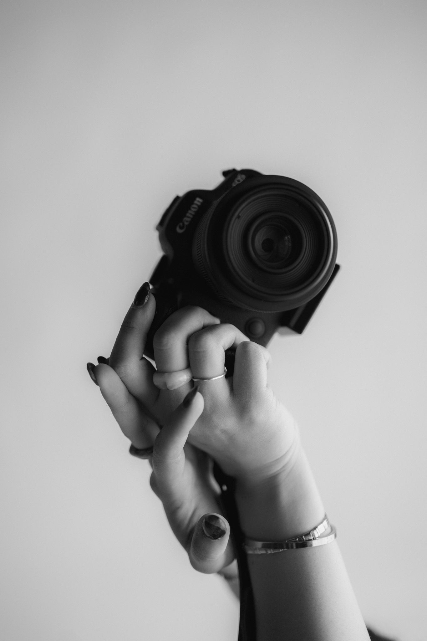 Black and white photo of hands holding a camera lens against a light background.