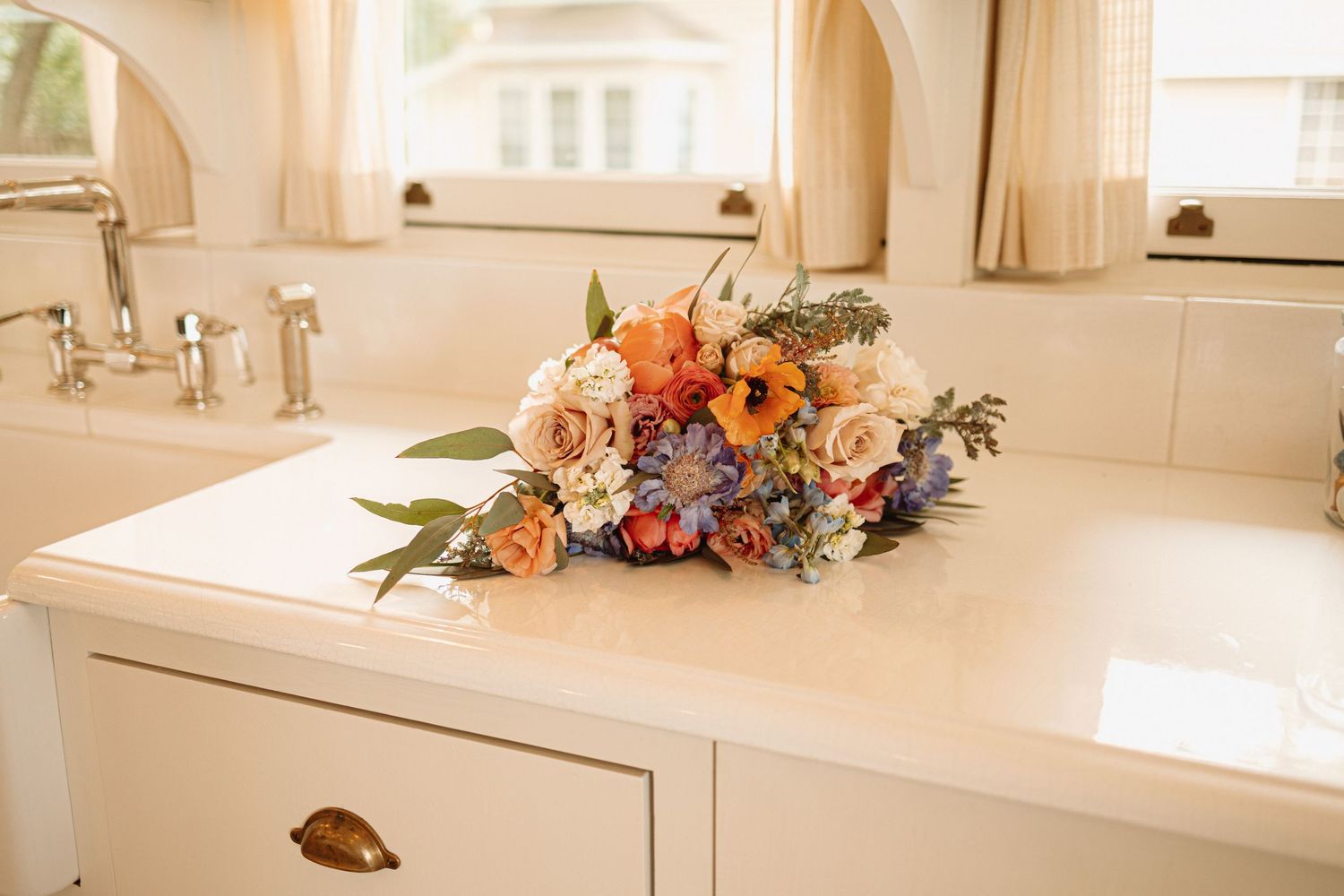 A modern white bathroom vanity features a floral arrangement with peach and coral flowers atop a quartz countertop.