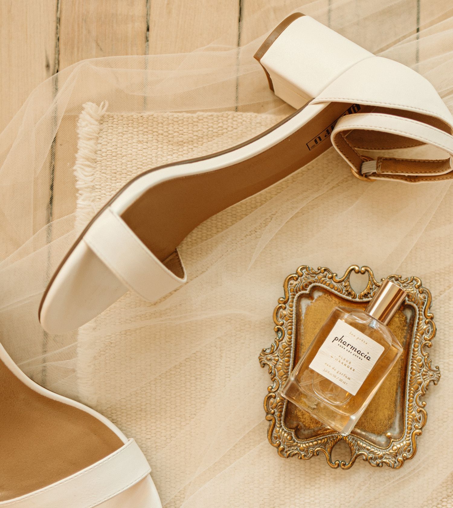 Luxury perfume bottle in ornate gold frame styled with white shoes and fabric on beige background.