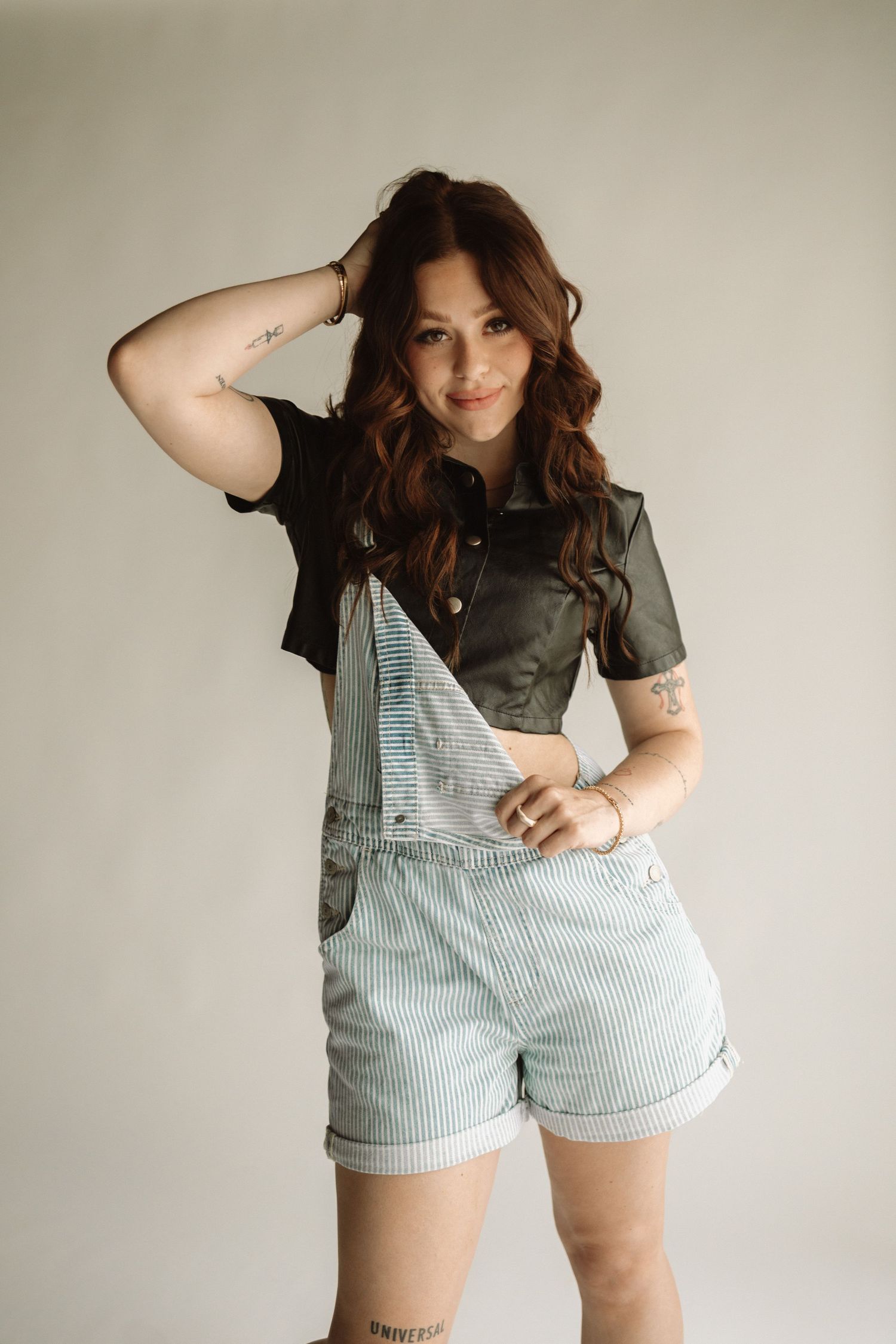 Fashionable outfit featuring striped blue and white overalls paired with a dark cropped shirt and rolled up shorts.