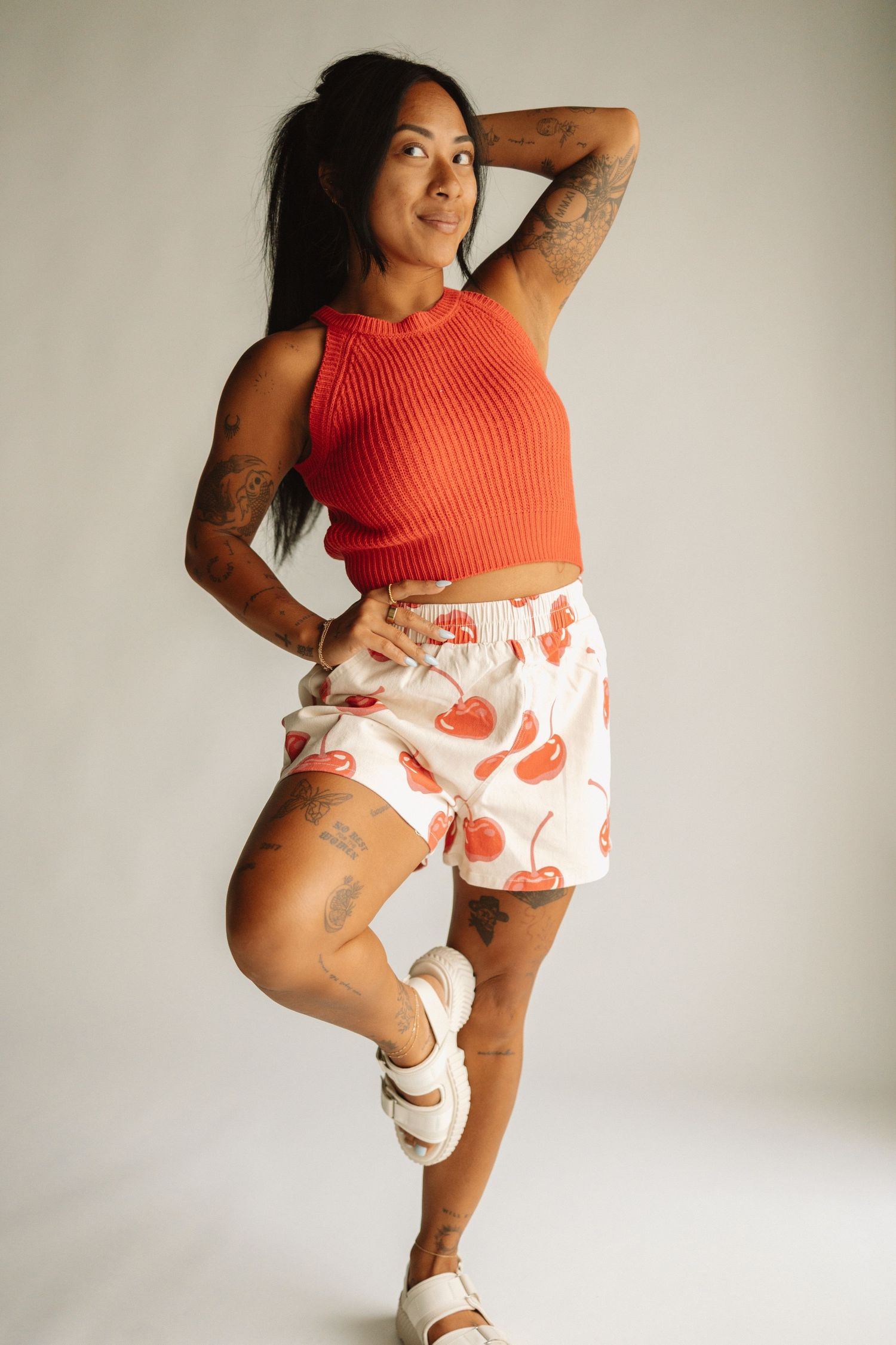 Woman in orange crop top and printed shorts strikes dynamic dance poses against white studio backdrop.