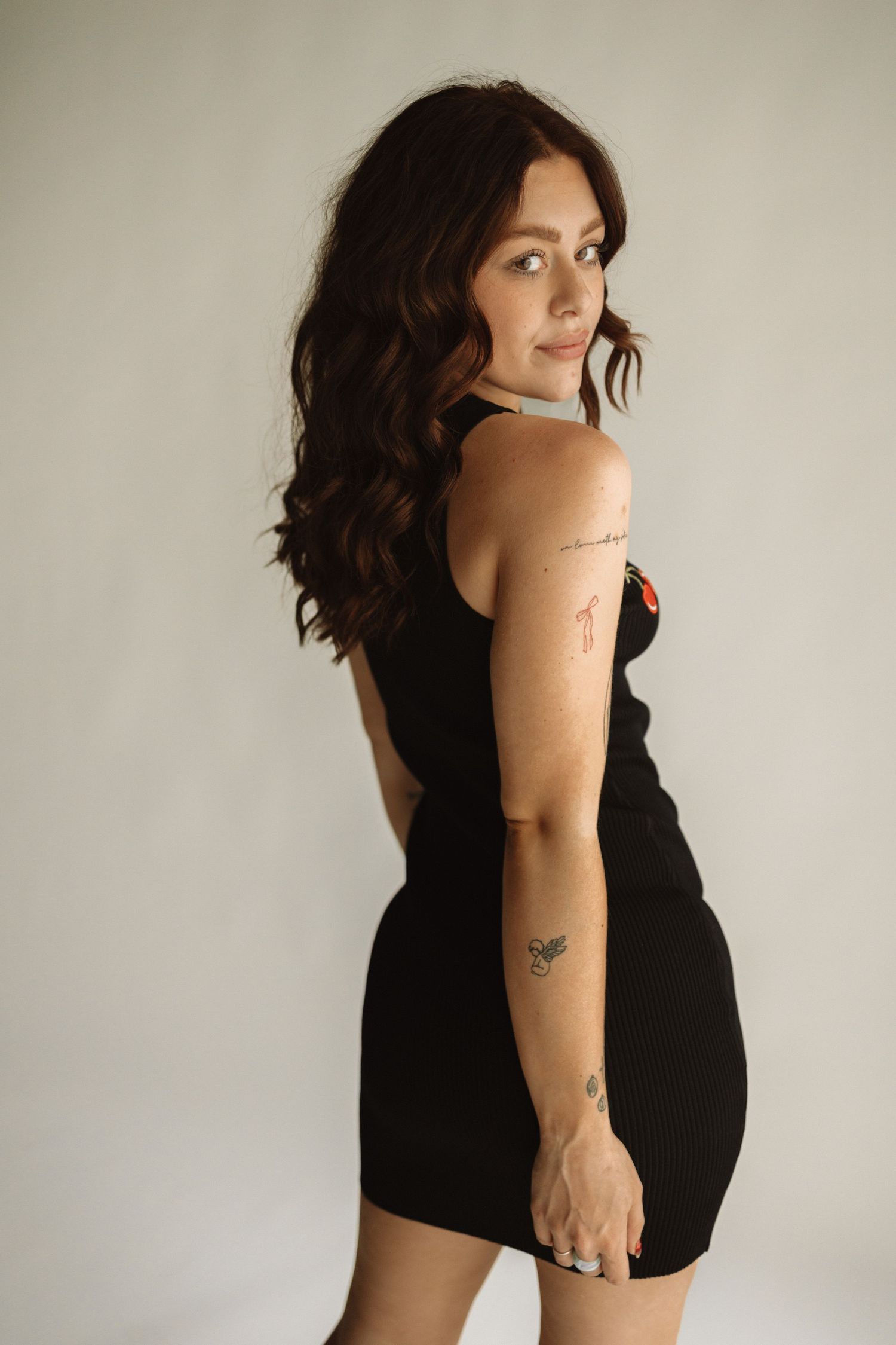 A woman in a black dress poses against a white wall in a series of artistic portrait photographs.