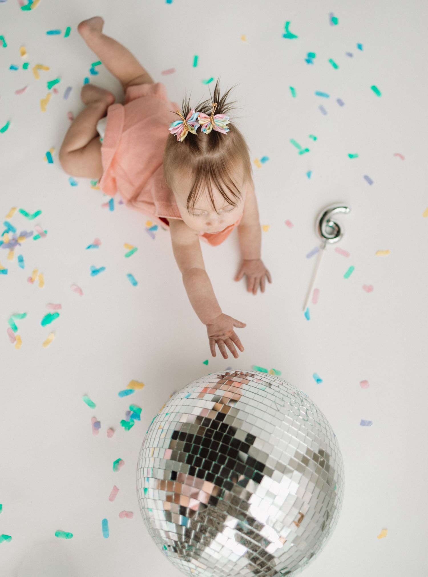 A disco ball reflects light while confetti falls against a white background in a celebratory party scene.