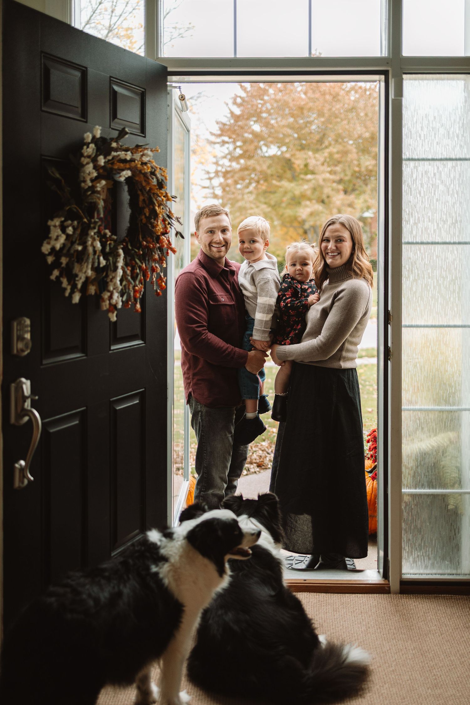 A group of people gather near a doorway with black and white dogs sitting in the foreground.