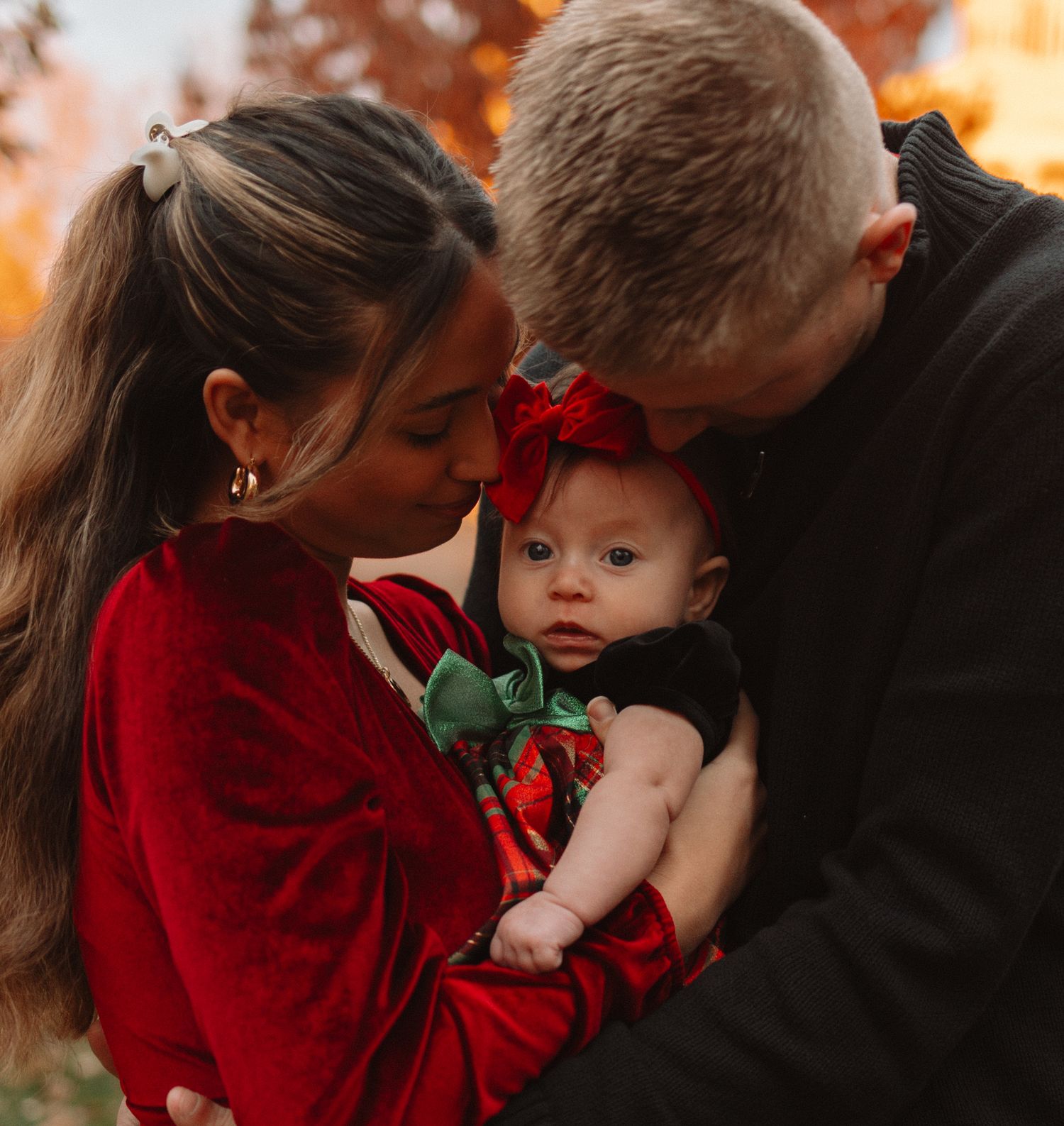 Family members in red and black clothing share tender moments during an autumn outdoor photo session.