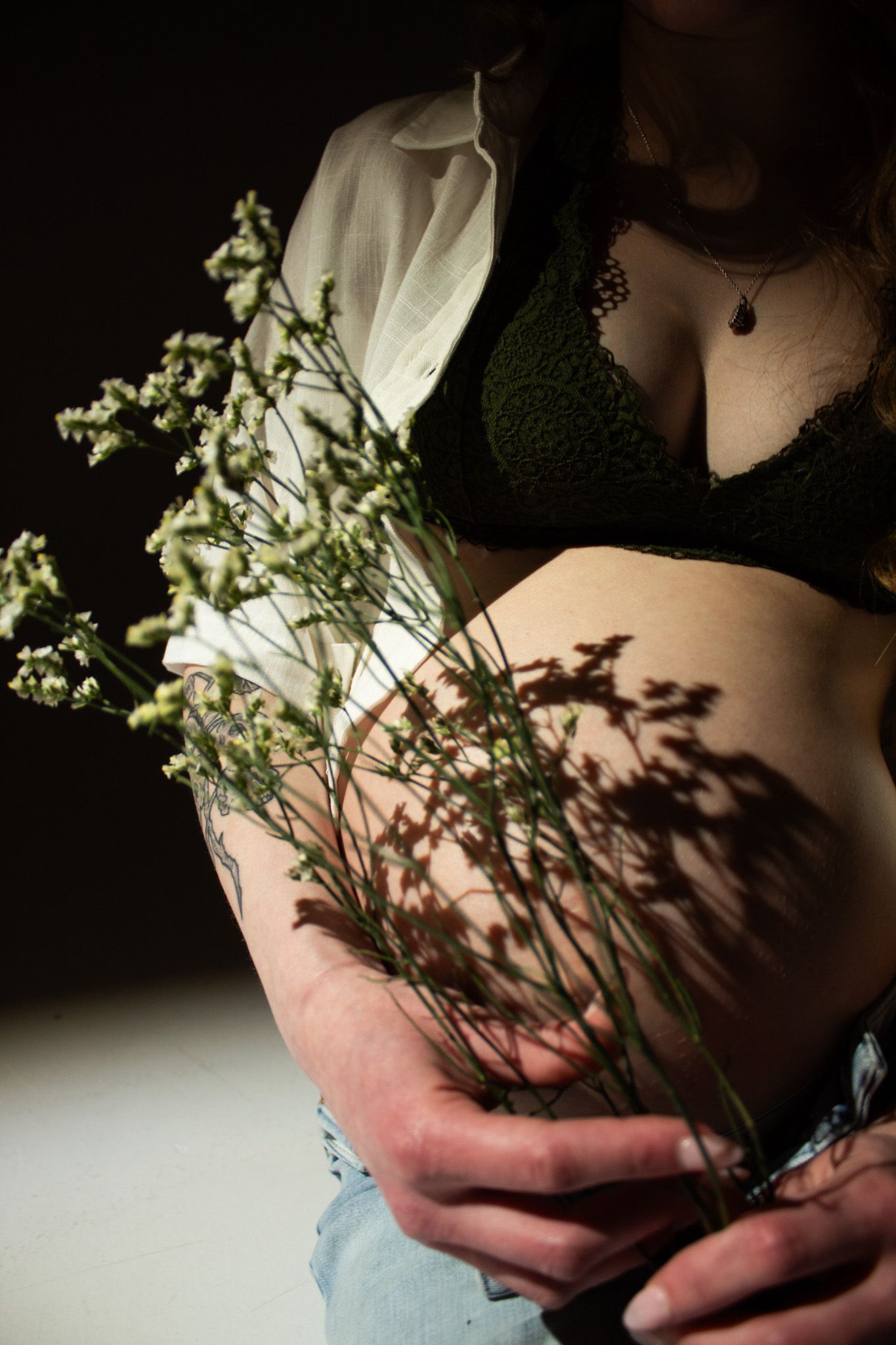 Hands holding delicate white flowers against dark background casting dramatic shadows in moody lighting.