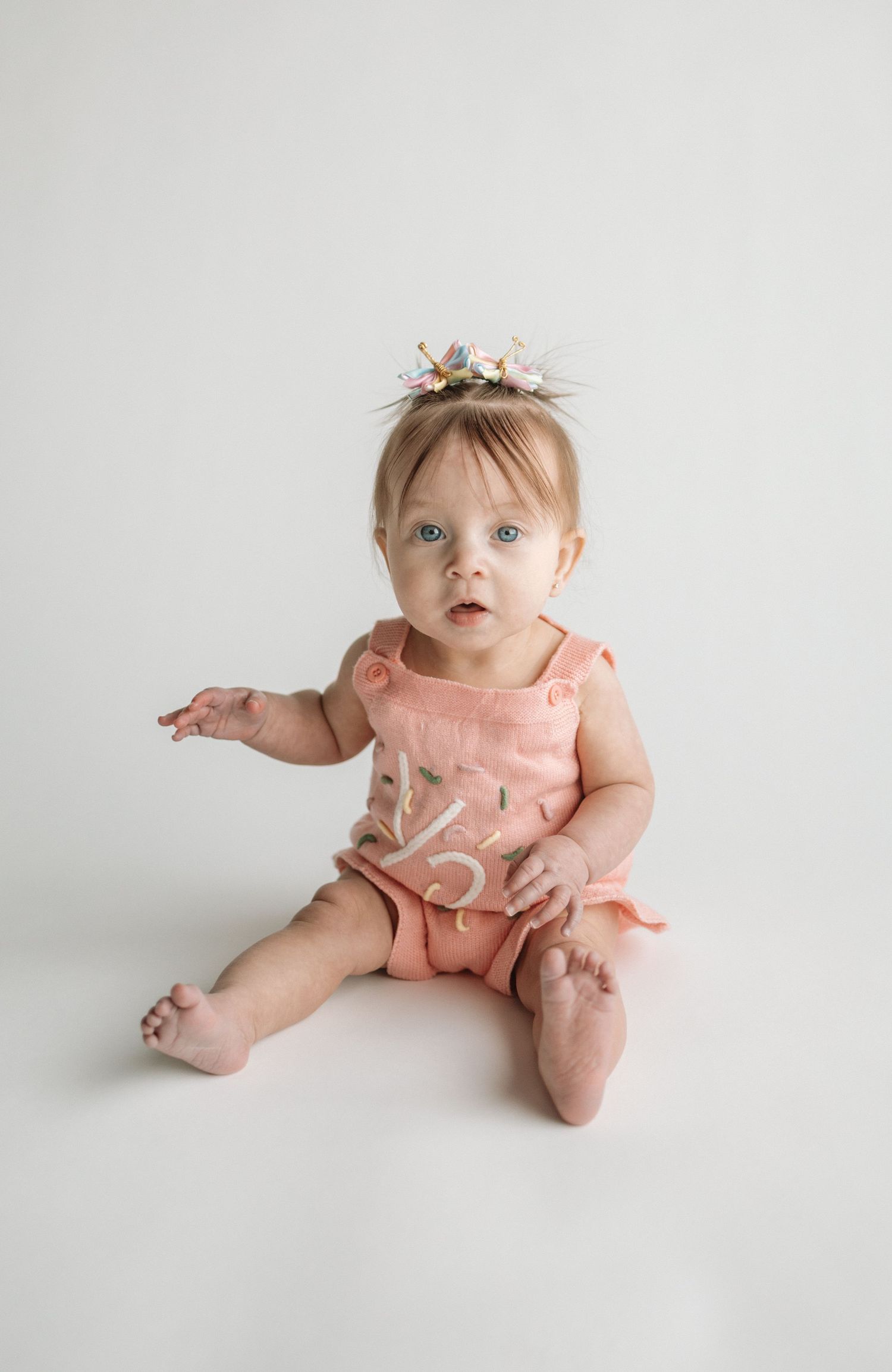 Baby in pink dress sits on white backdrop showing progression of movement in three connected photos.