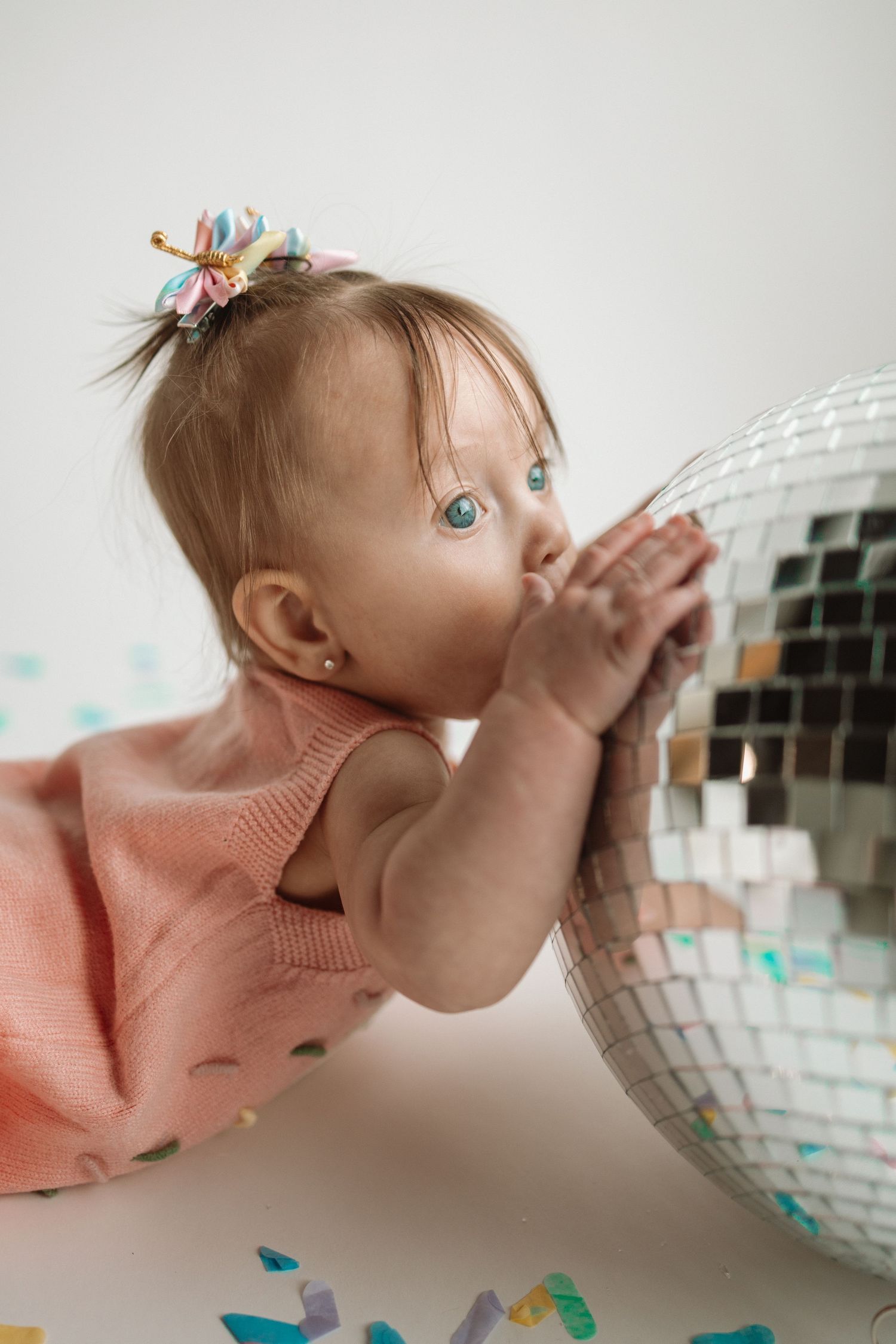 A child in a pink sweater playfully kisses a shiny disco ball in a series of three sequential photos.