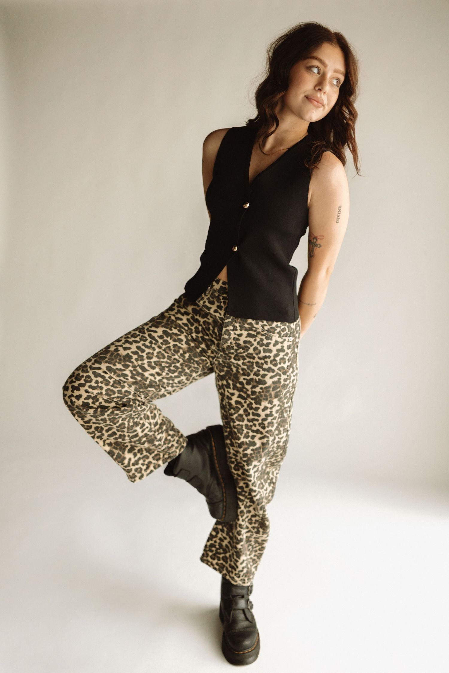 Fashion model poses in black vest top with leopard print wide leg pants and combat boots against white studio background.