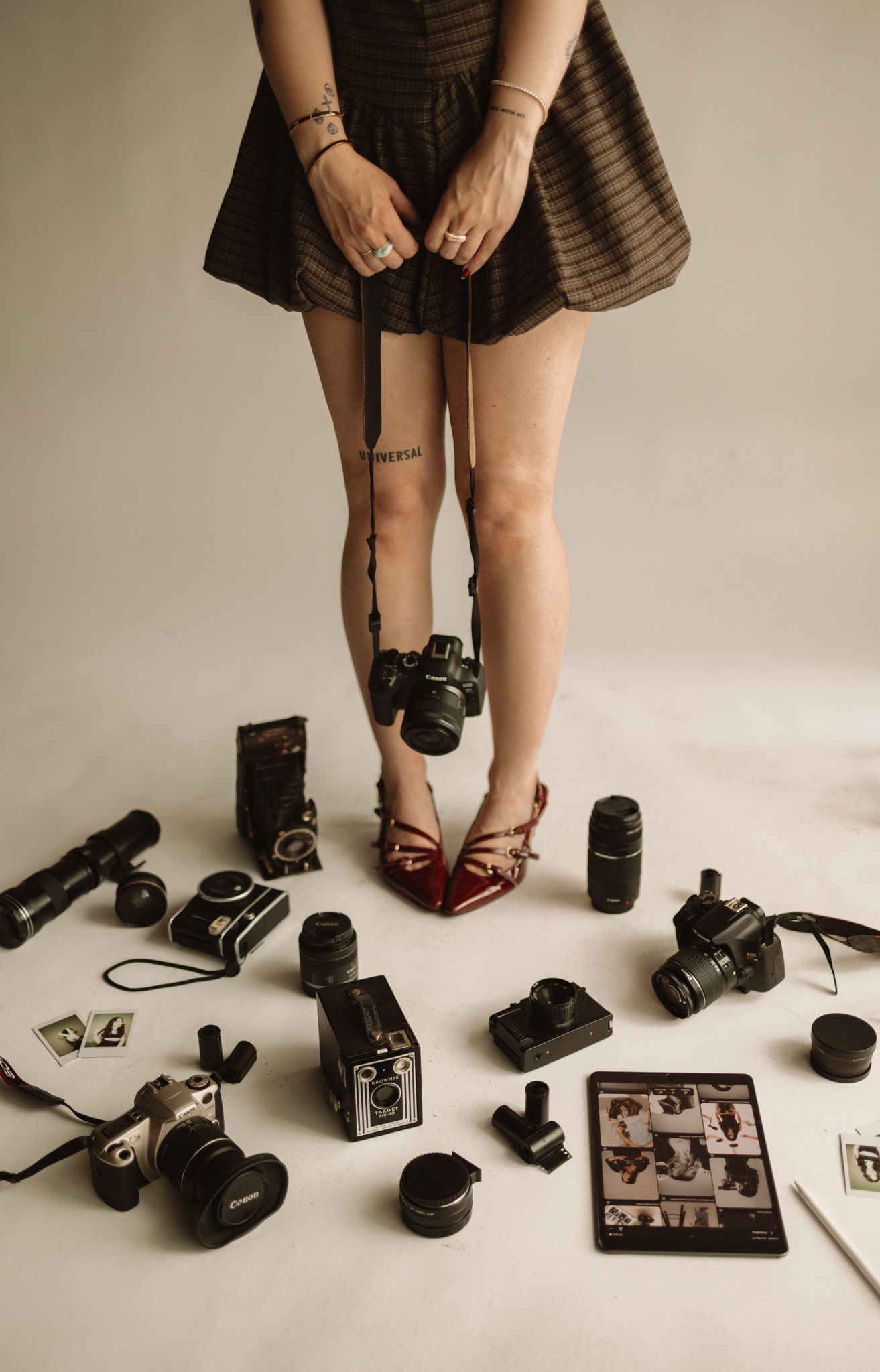 A sequence of vintage cameras and photography equipment arranged with legs and red shoes visible in the background.