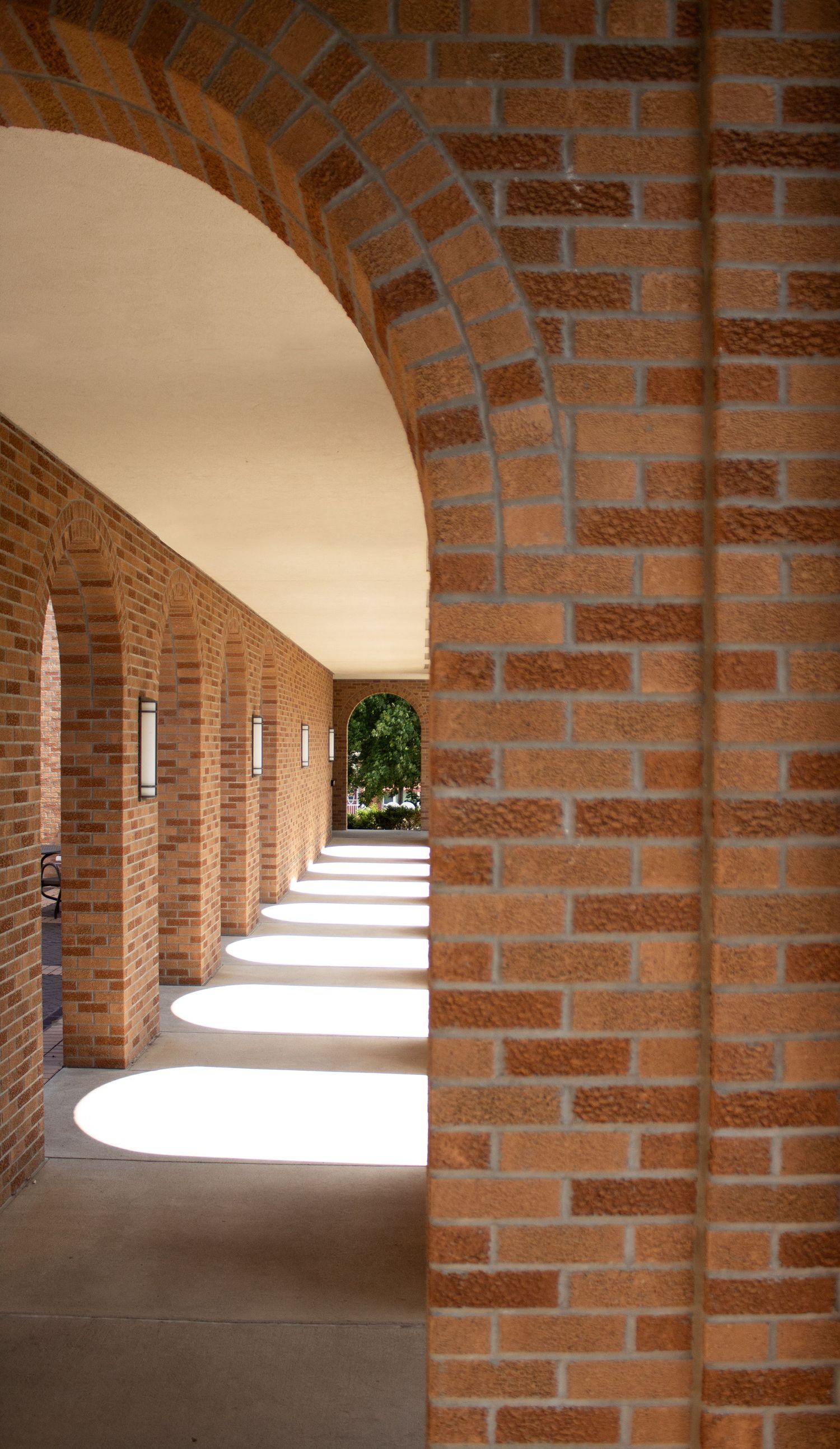 Sunlight streams through a series of brick archways in a covered walkway creating dramatic shadows and patterns.