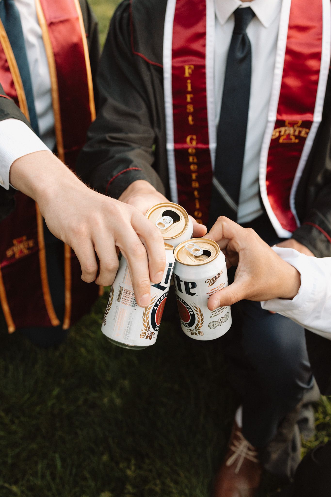 Close-up of graduation stoles and hands toasting with Miller Lite beer cans.