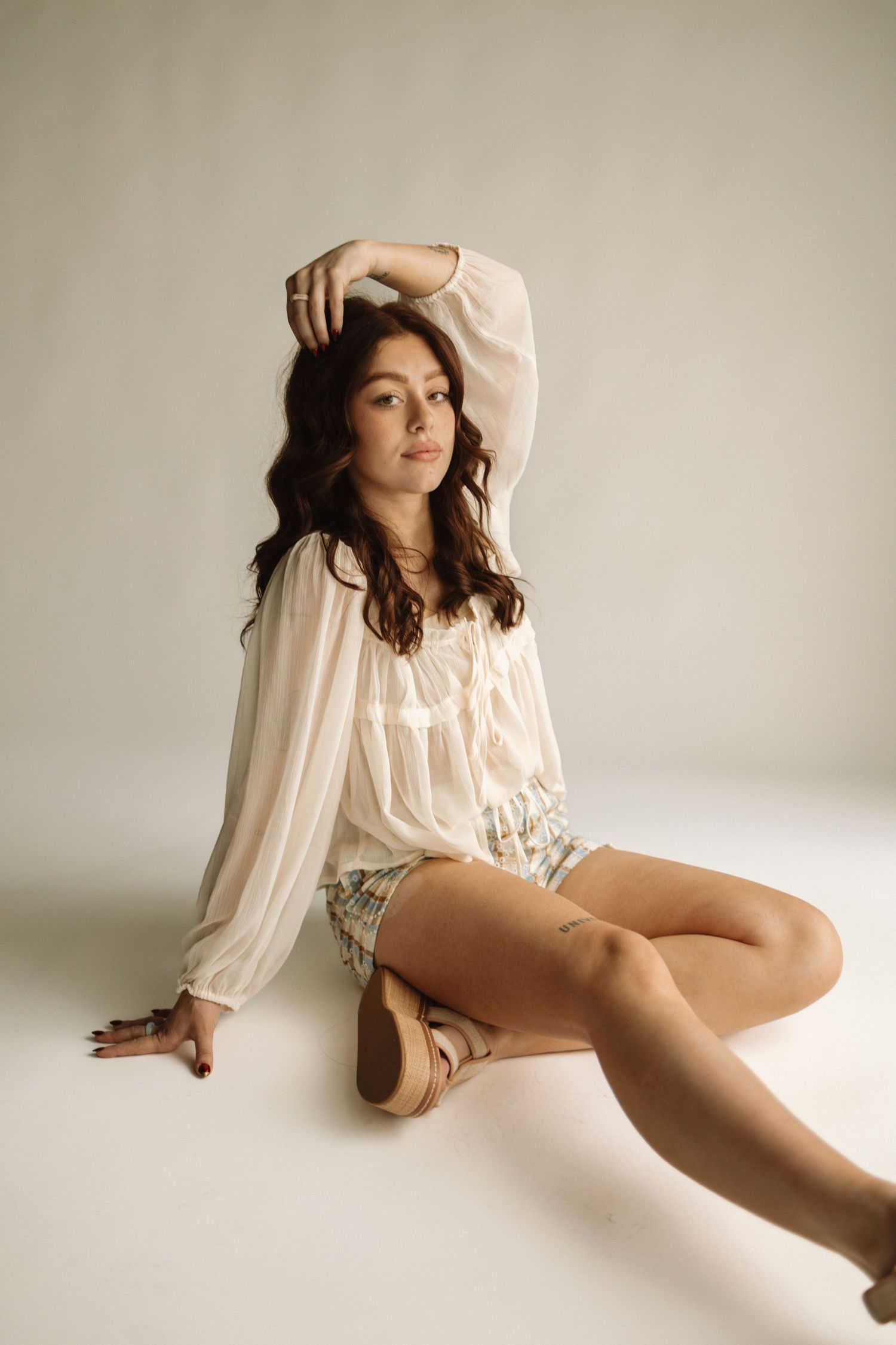 A person in a flowy cream blouse and shorts poses gracefully against a white studio backdrop.