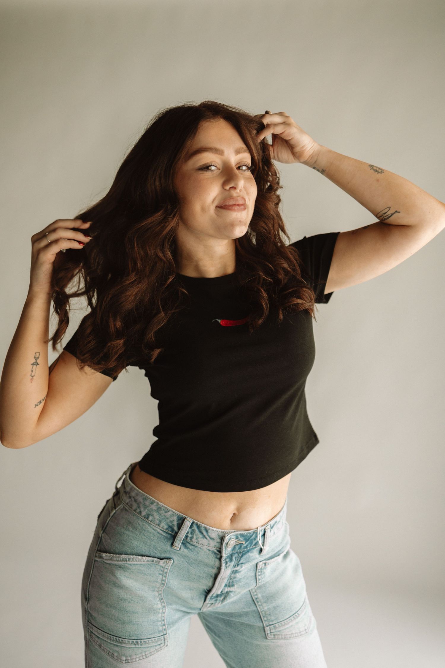 Person in black crop top and light wash jeans posing artistically against white wall in fashion photoshoot series.