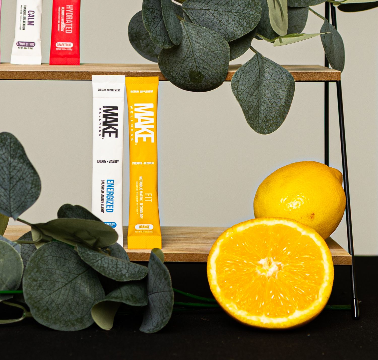 Fresh orange slices arranged on a wooden surface next to green eucalyptus leaves and white storage containers.