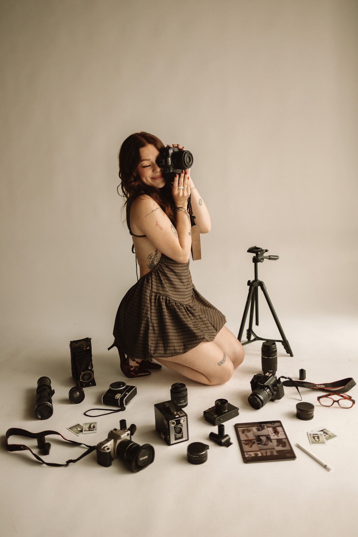 Photographer surrounded by professional camera equipment including lenses, tripod and accessories on white background.