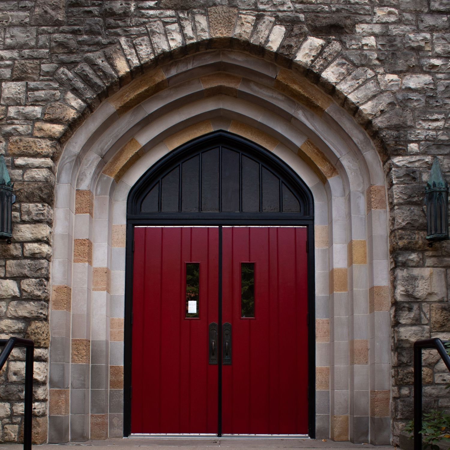 An arched Gothic stone doorway with bright red double doors and decorative stonework details.