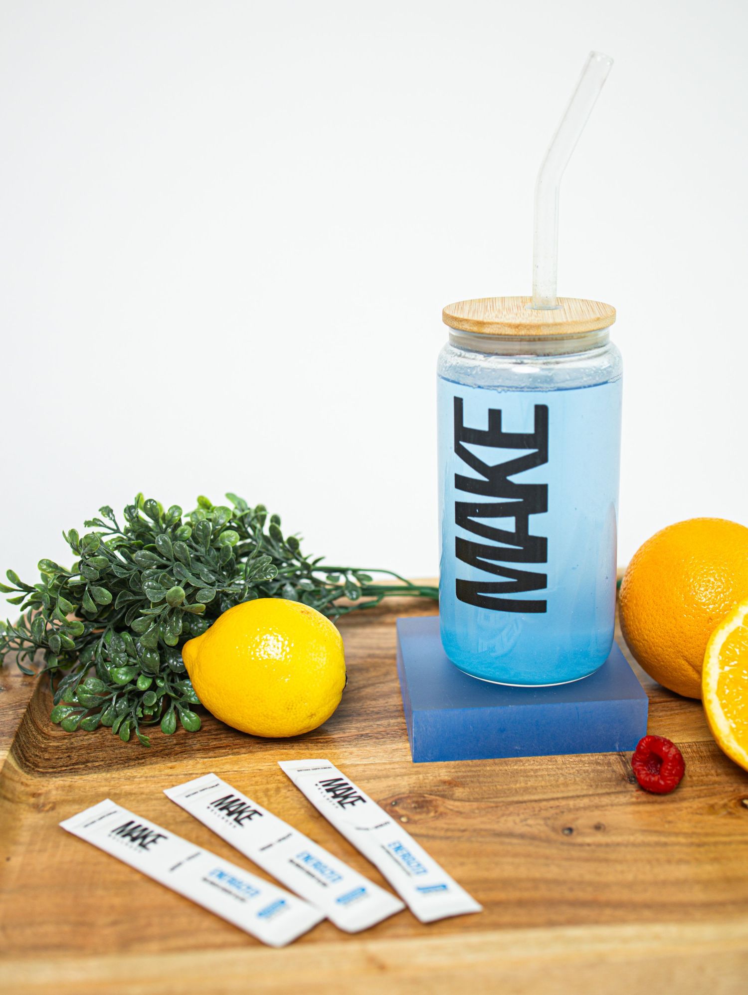 A blue gradient cocktail in a glass sits on a wooden surface with citrus fruits and fresh herbs as garnish.