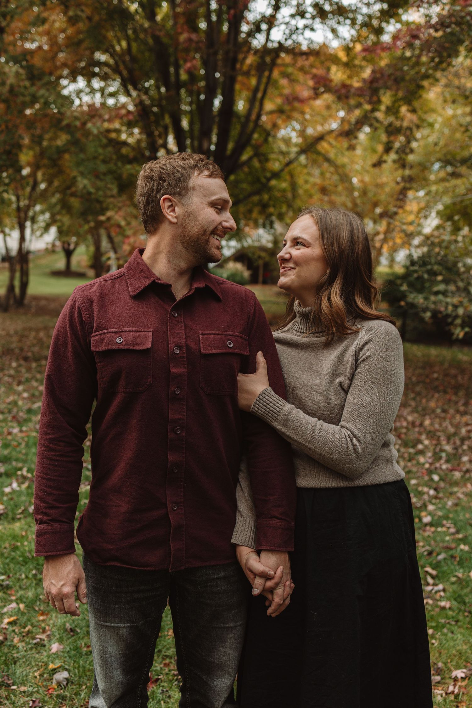 A couple shares a joyful moment together in an autumn park with colorful fall foliage in the background.
