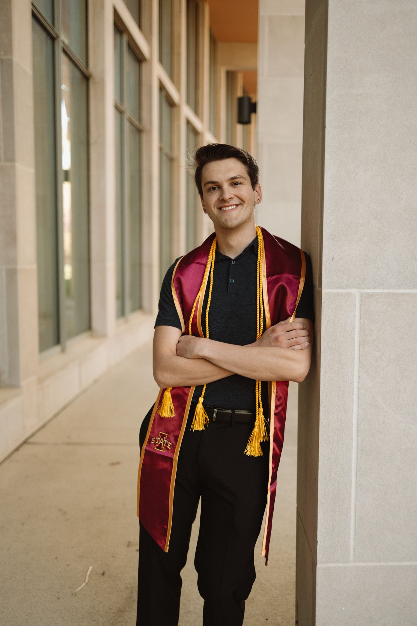 Graduate wearing maroon and gold stole posing against a light colored hallway with columns.