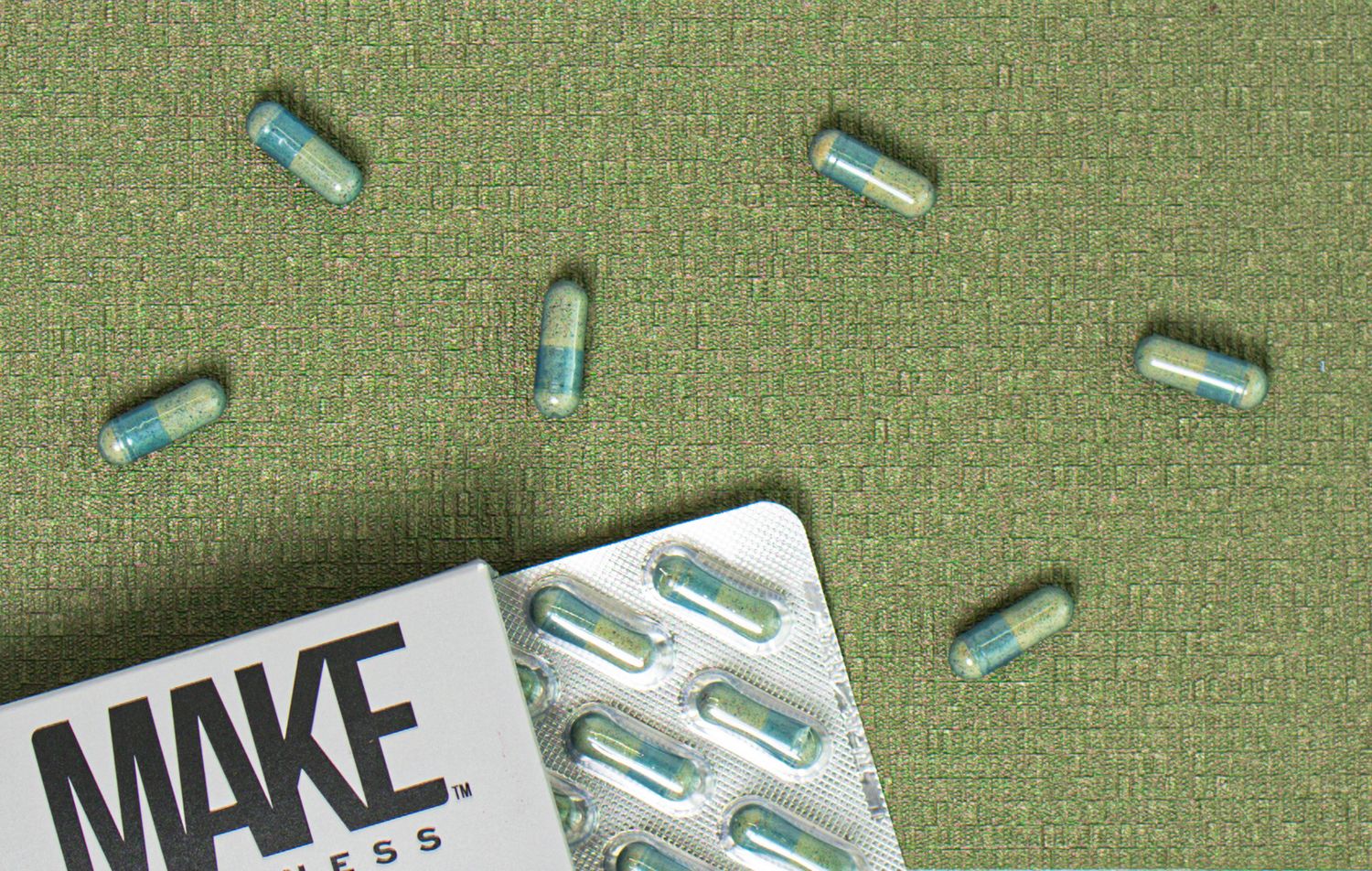 Several blue and white capsule pills scattered on a green surface next to a medication package.