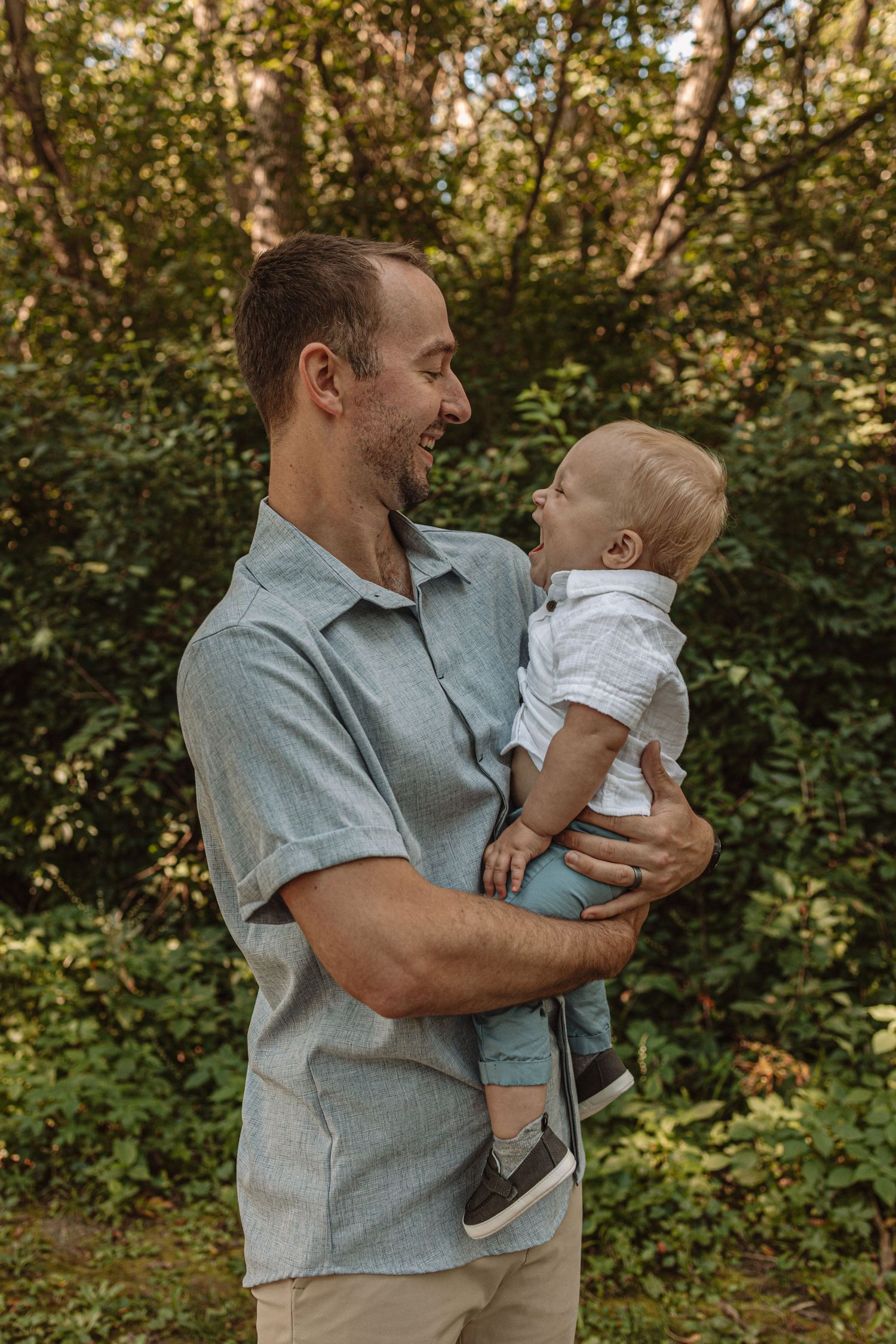A tender moment captured in nature as an adult holds a small child against a backdrop of lush green foliage.