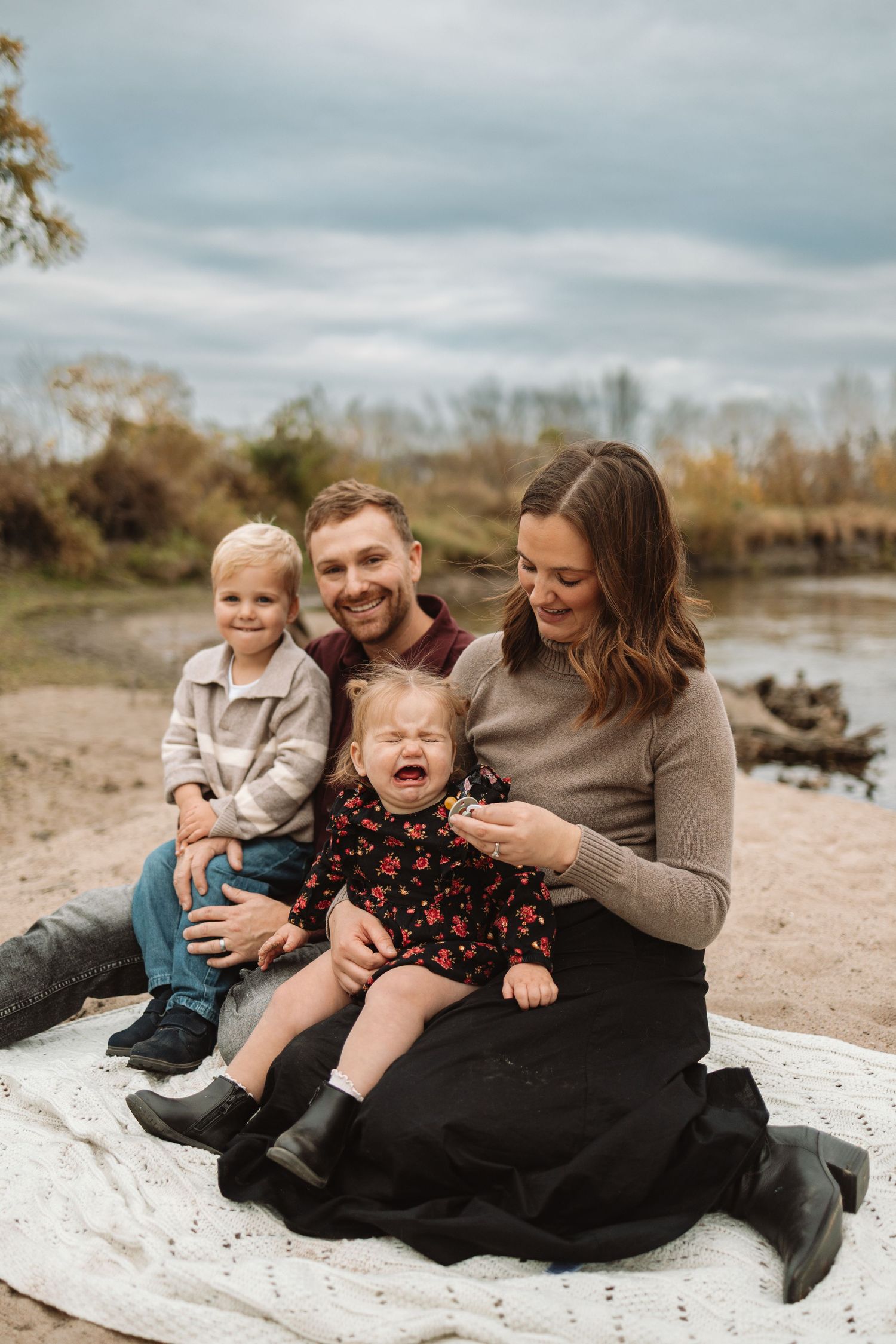 Family enjoying a casual autumn day sitting together on a blanket by the water's edge.