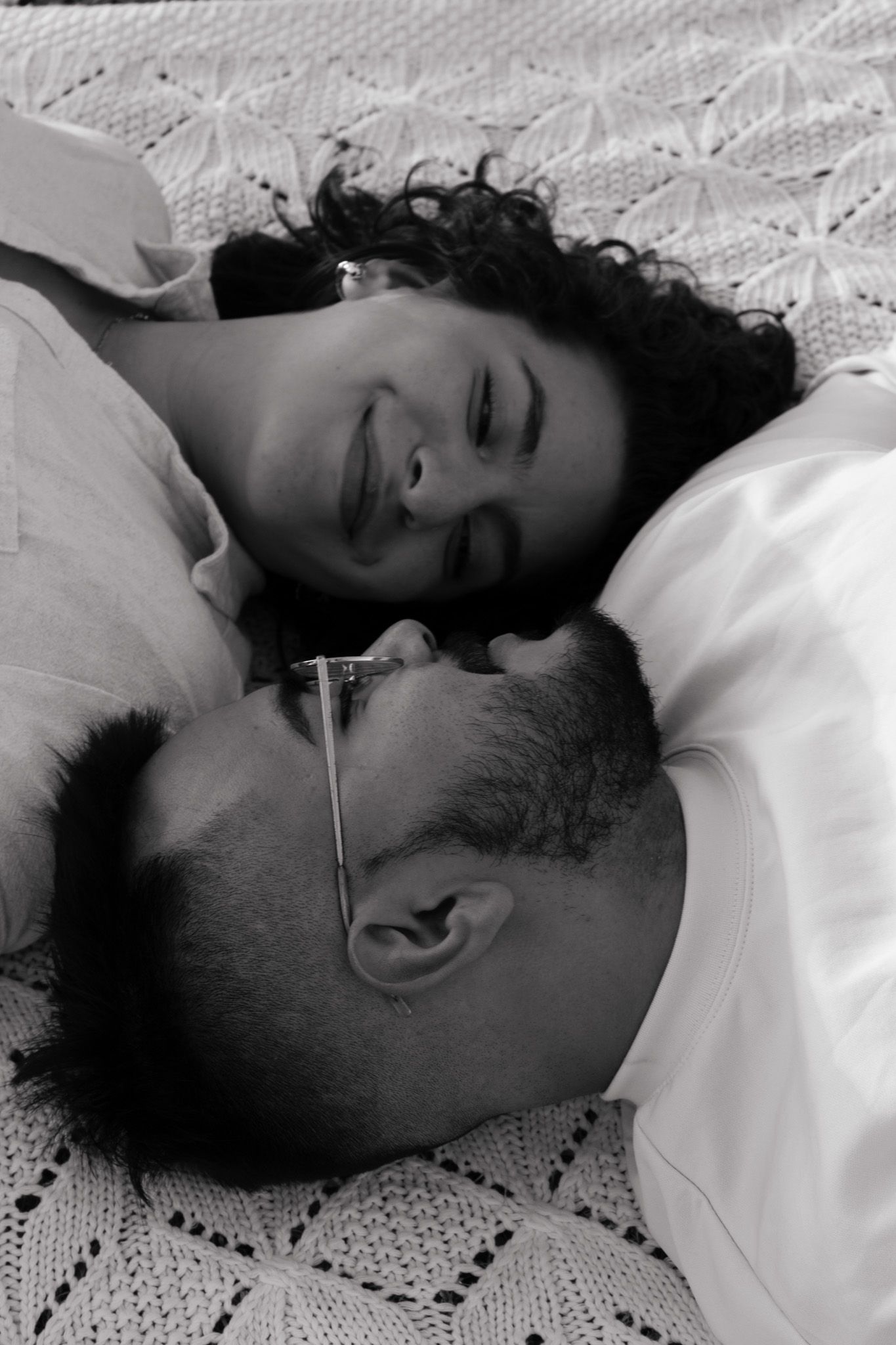 Romantic black and white portrait of couple lying close together on lace bedding.