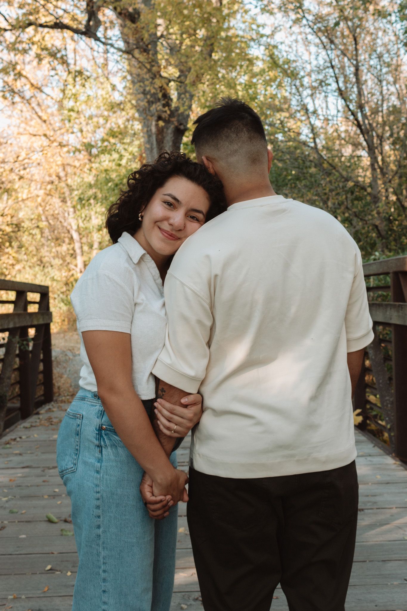 Romantic couple sharing an intimate moment together on a wooden bridge surrounded by autumn trees in golden light.