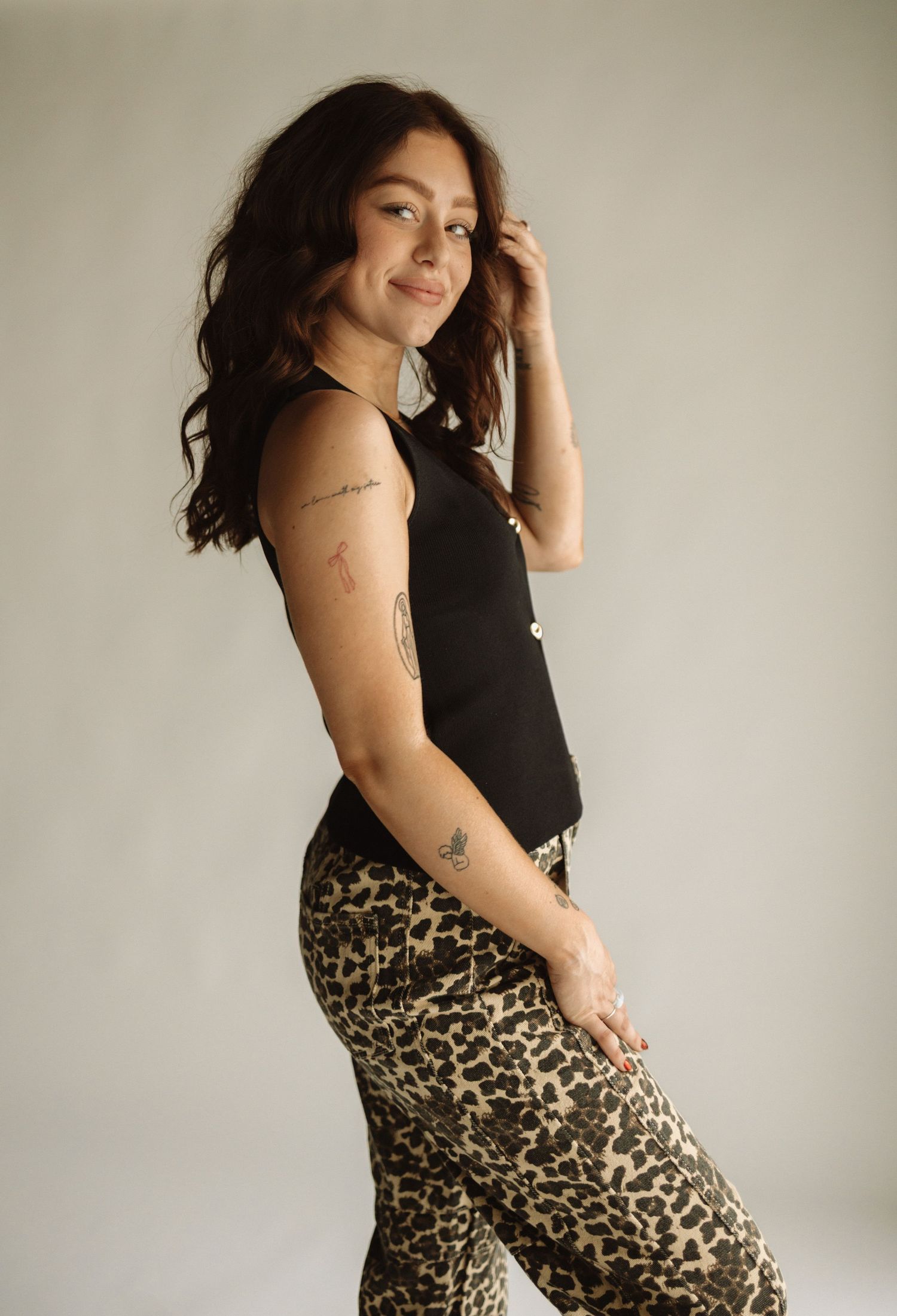 Person in black top and leopard print pants poses confidently against neutral wall in fashion photoshoot series.