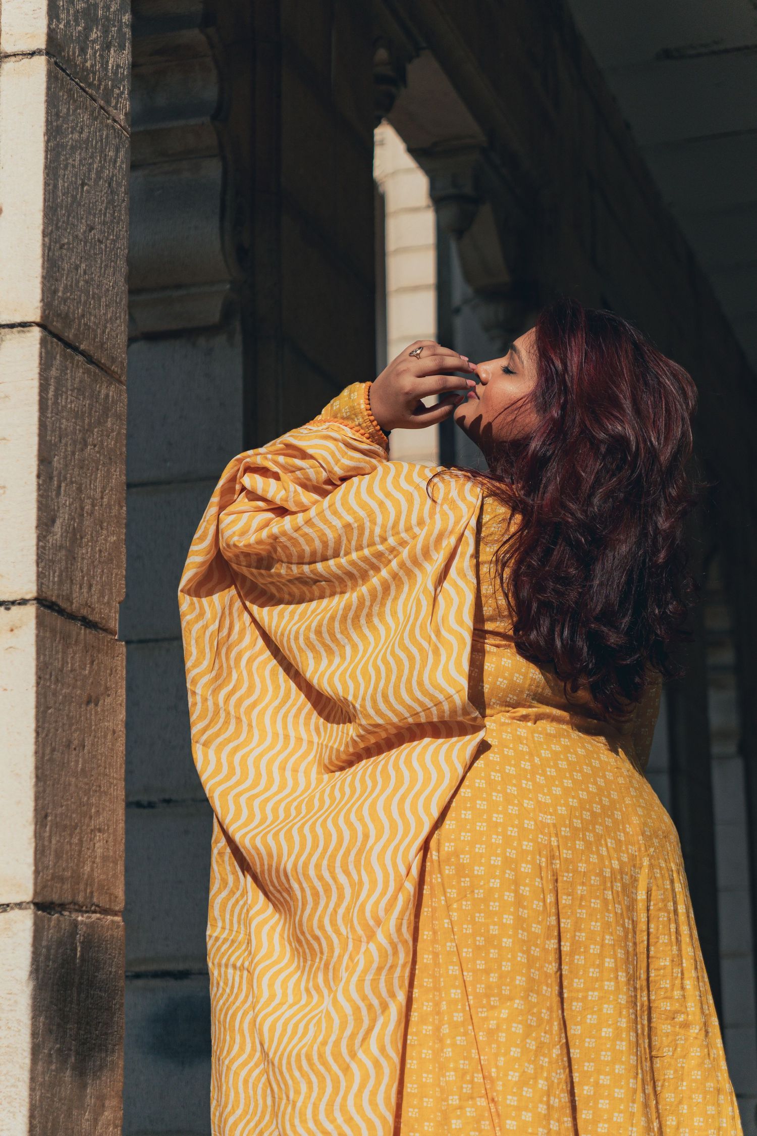 Modern Indian look of women doing hair flip in yellow dress in historical palace in Vadodara, Gujarat, India