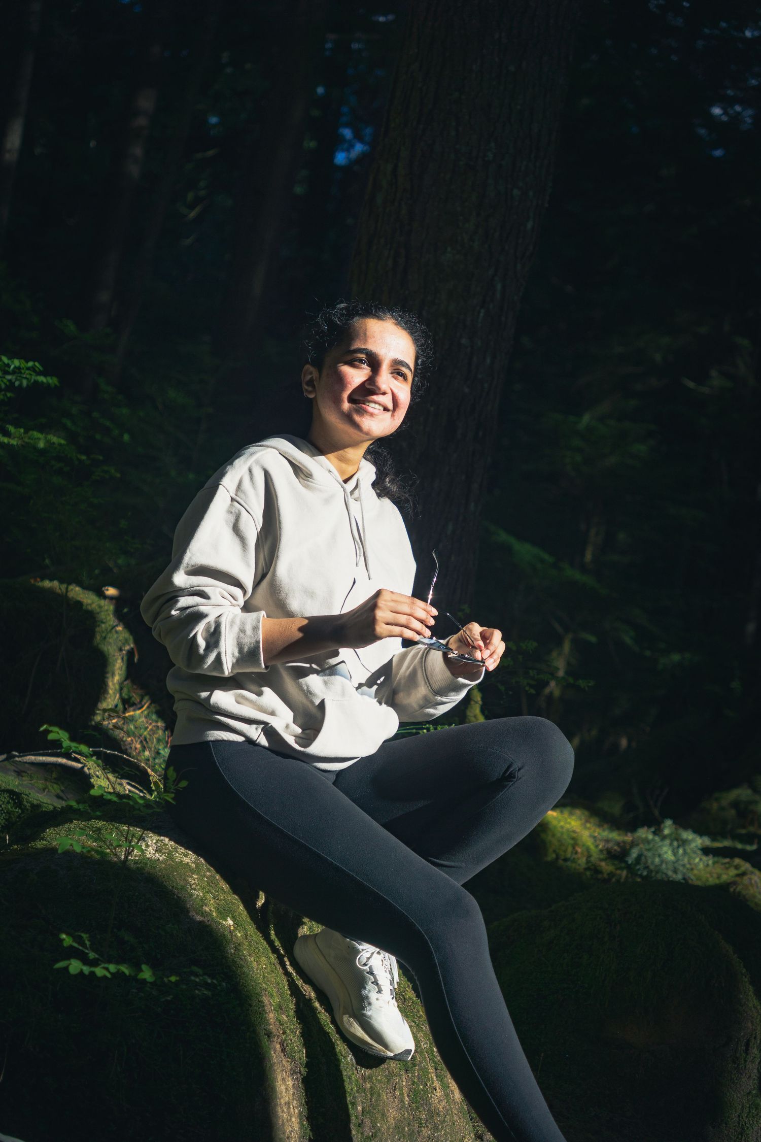Sunlight hitting through the trees onto a woman candidly smiling on a hike on a sunny afternoon in Buntzen lake, Vancouver