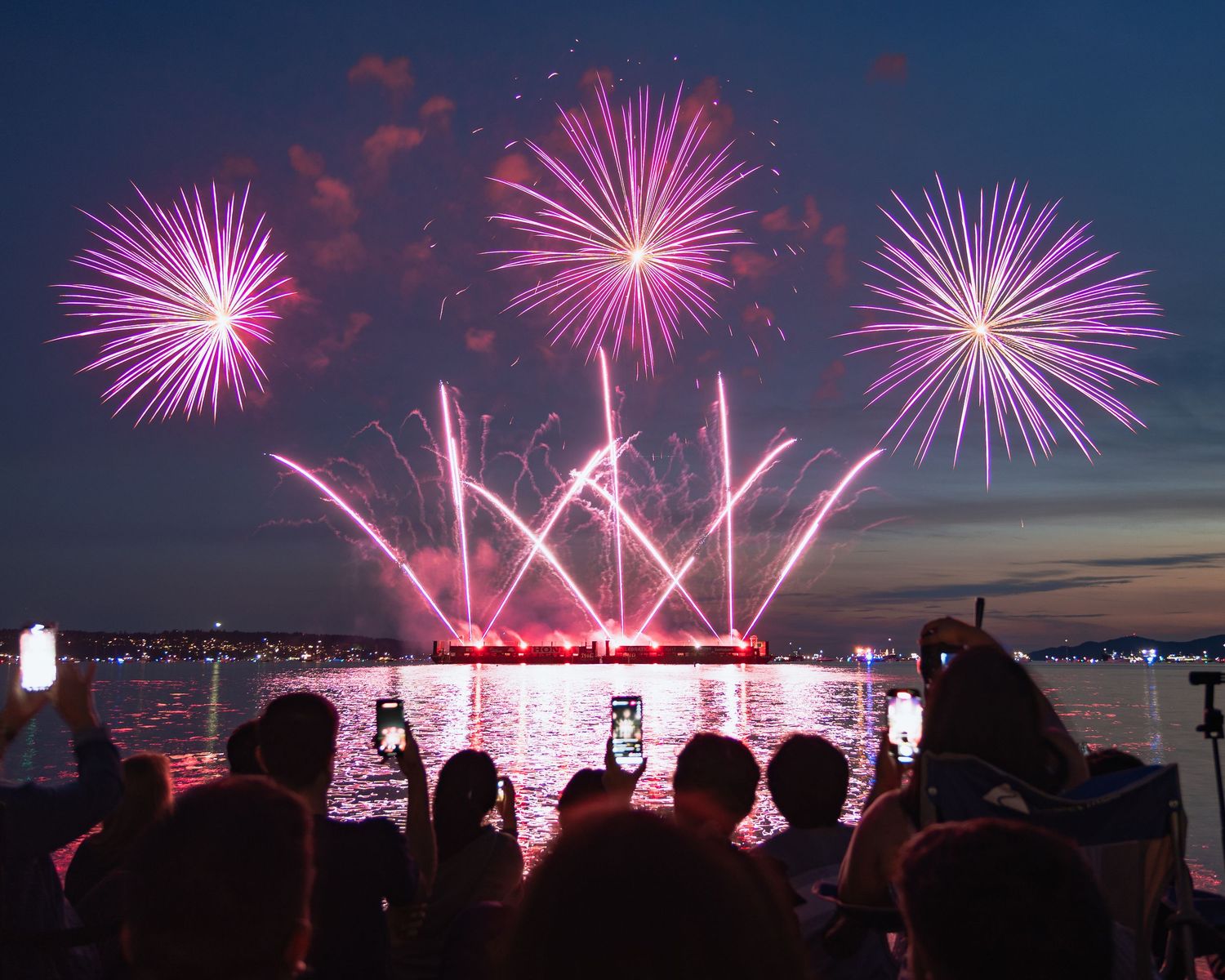 Pink/purple firework burst illuminating clouds at night in English Bay
