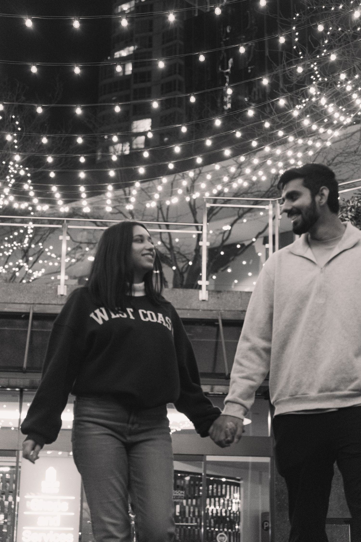 Romantic couple standing behind string lights in a dimly lit alley at night in Vancouver, Canada