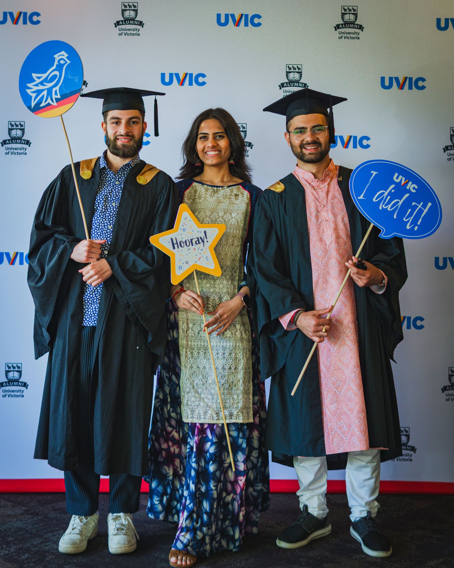 University of Victoria graduates posing with props with UVic backdrop