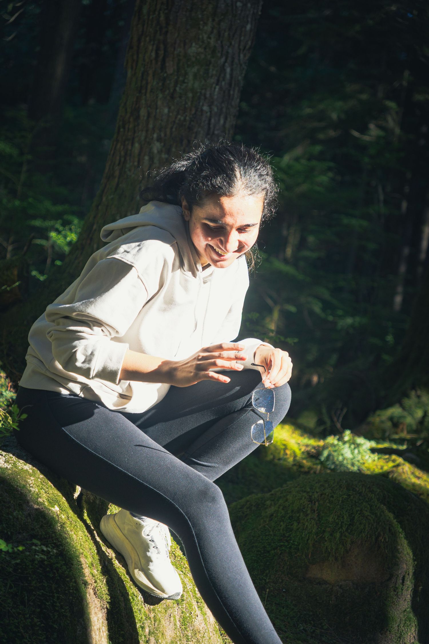 Natural portrait through the trees onto a woman candidly laughing on a hike on a sunny afternoon in Buntzen lake, Vancouver
