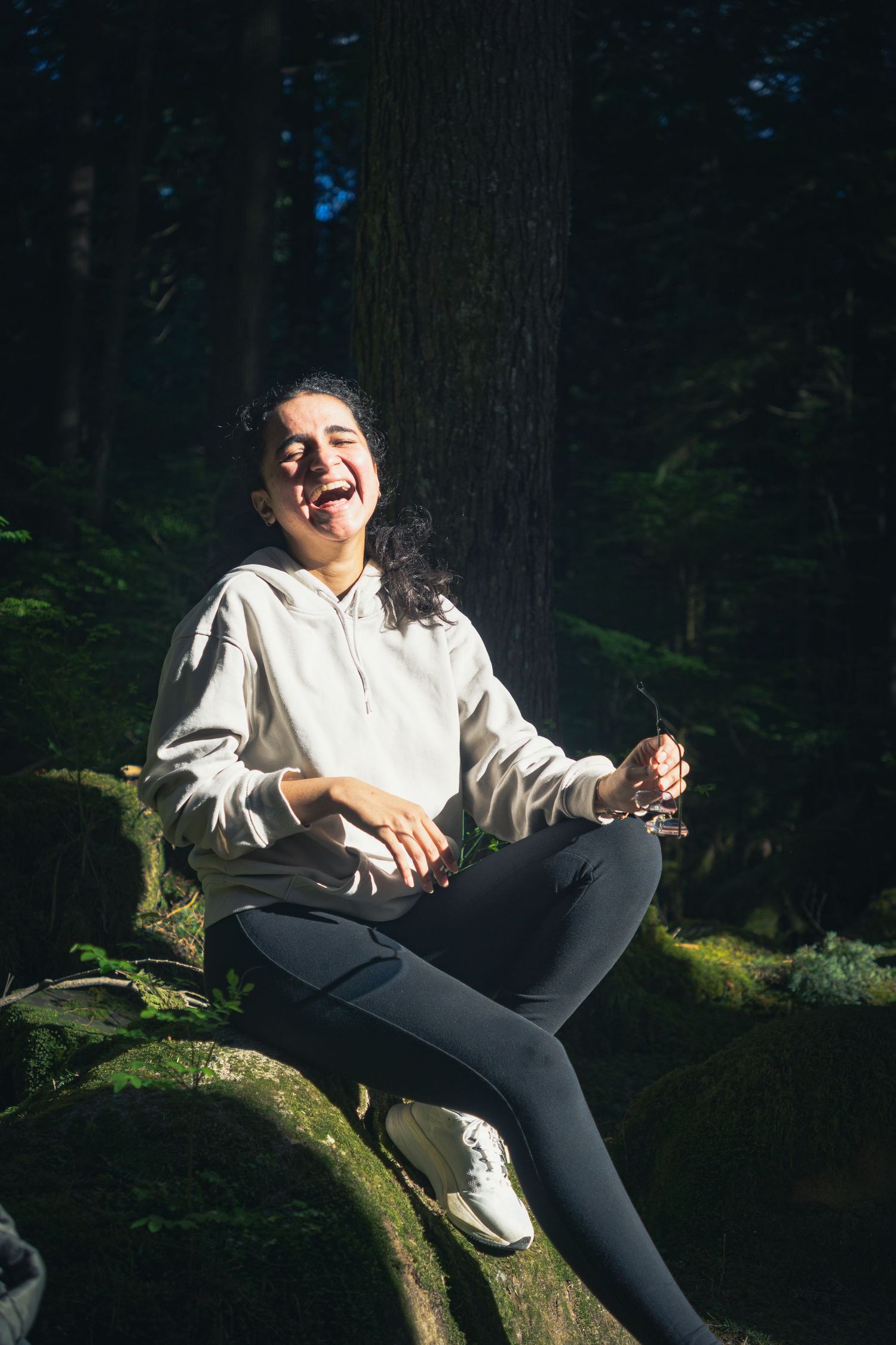 Sunlight hitting through the trees onto a woman candidly laughing on a hike on a sunny afternoon in Buntzen lake, Vancouver