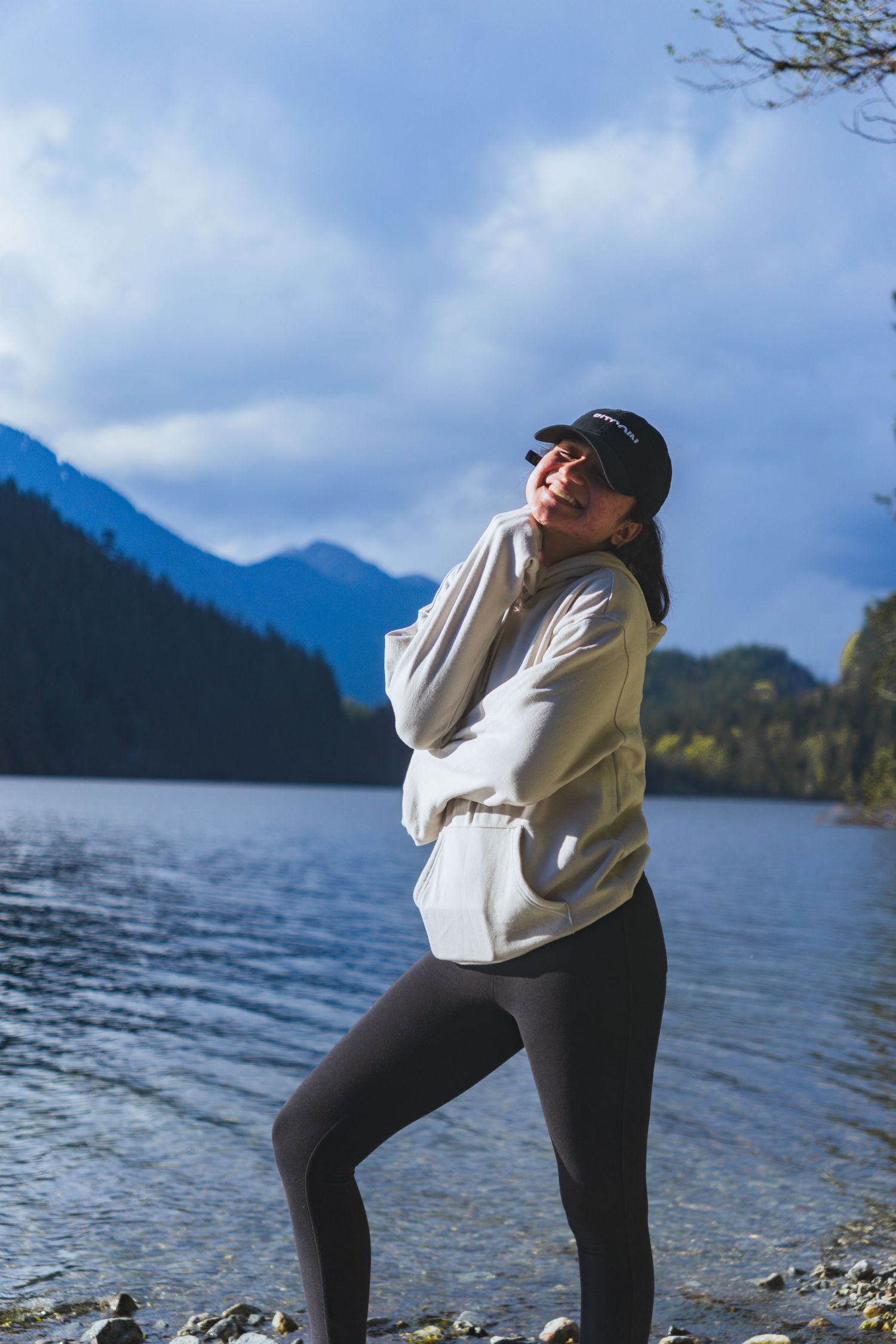 Women candidly posing with a buntzen lake background and mountains in a hoodie on a sunny afternoon in Buntzen lake, Vancouver