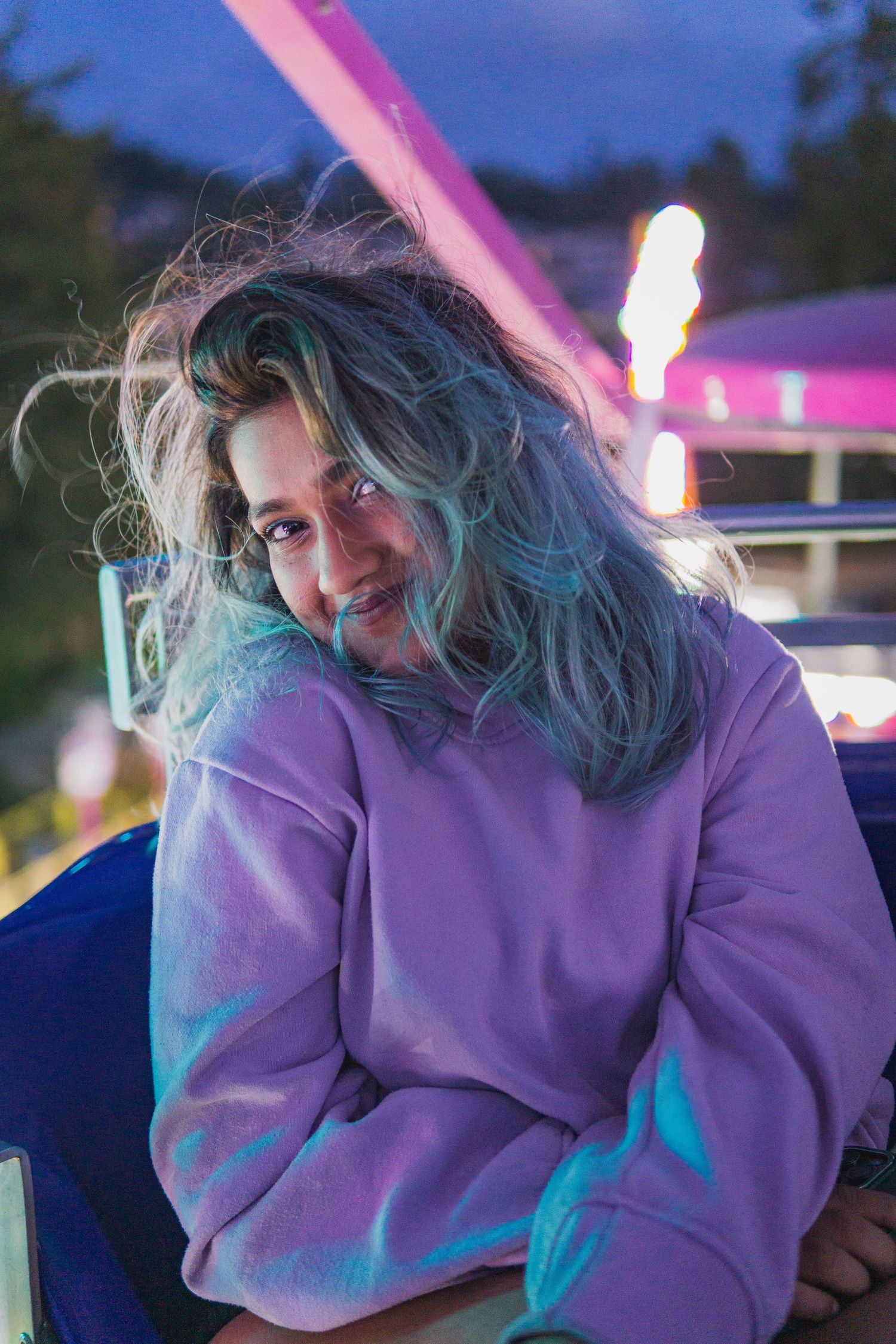 Woman posing in purple hoodie enjoying nighttime fair under colorful lights in Victoria, Canada