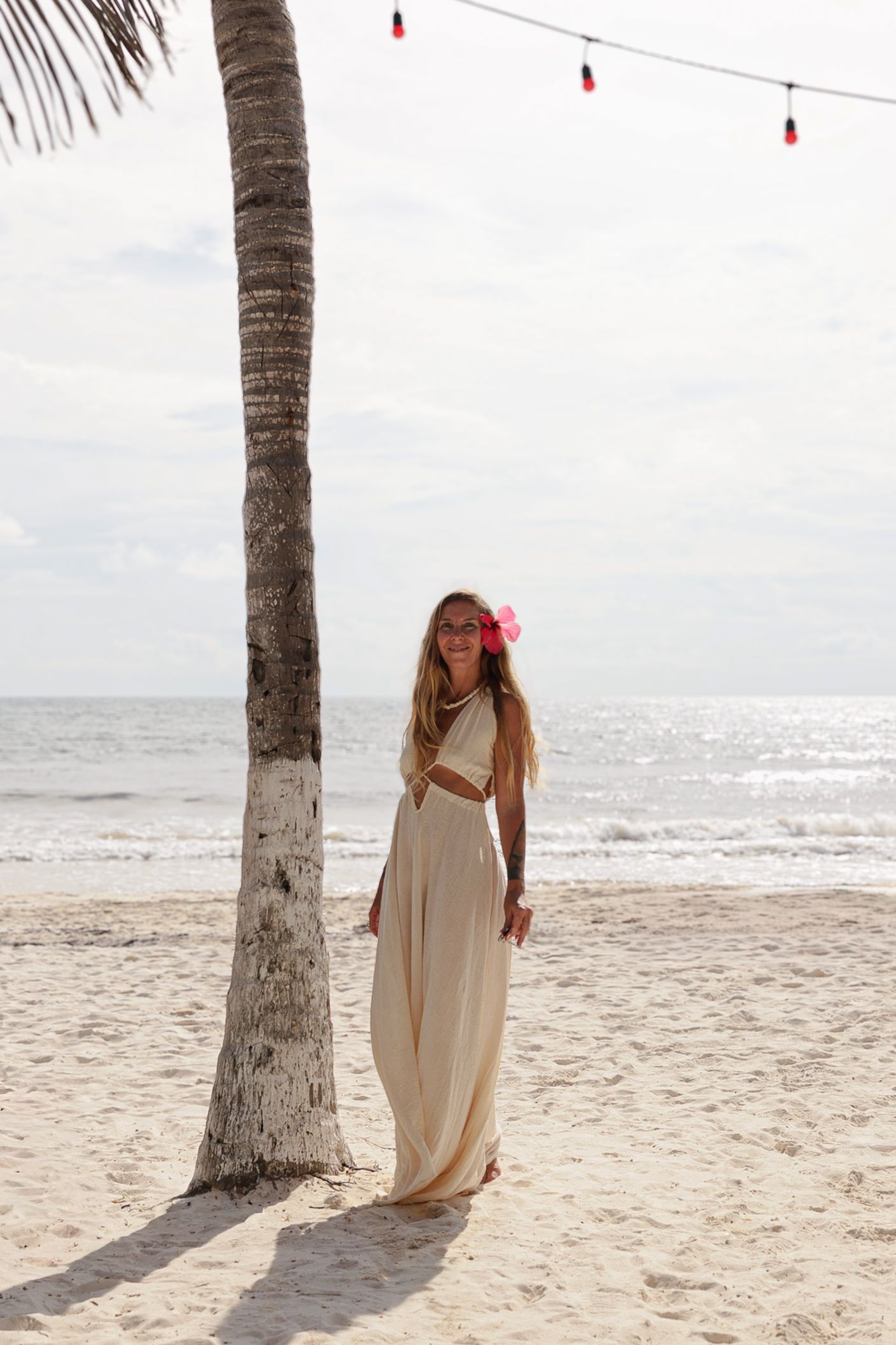 fotografia lifestyle. una modelo en la playa con vestido blanco junto a una palmera, detras se ve el mar