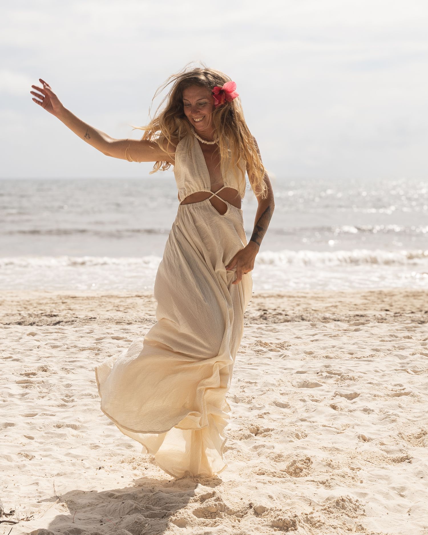 fotografia lifestyle. una modelo en la playa con vestido blanco generando un salto en el lugar, detras se ve el mar
