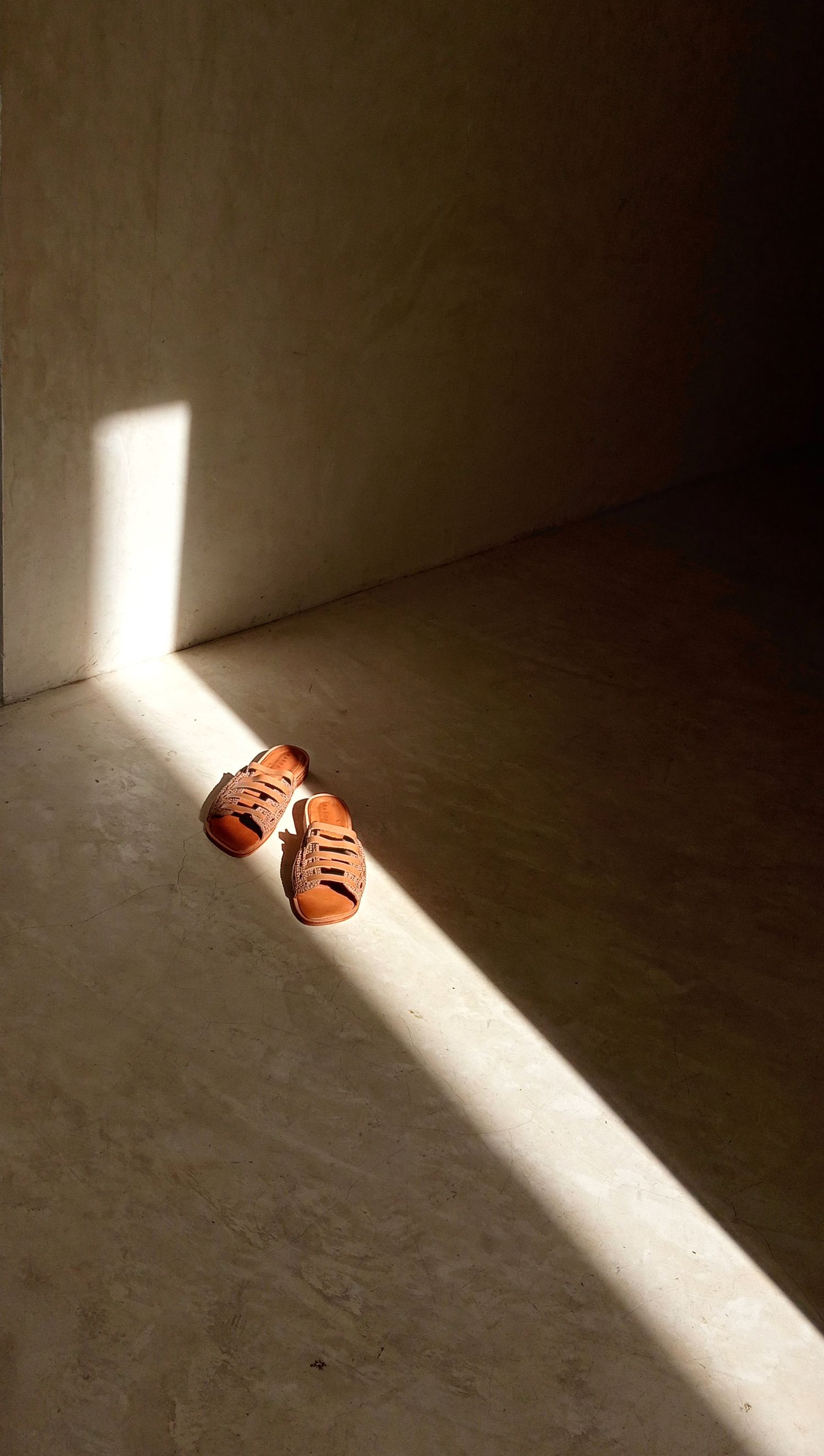 Fotografia de produto un rayo de luz que se reflena en el piso y atravisa un par de sandalias de cuero dejandolass visibles