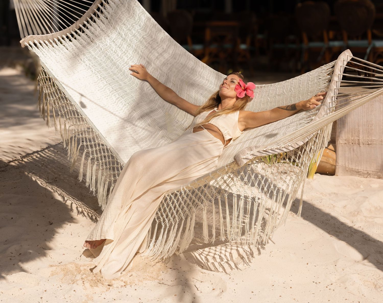 fotografia lifestyle. una modelo recostada en una hamaca en la playa con vestido largo blanco