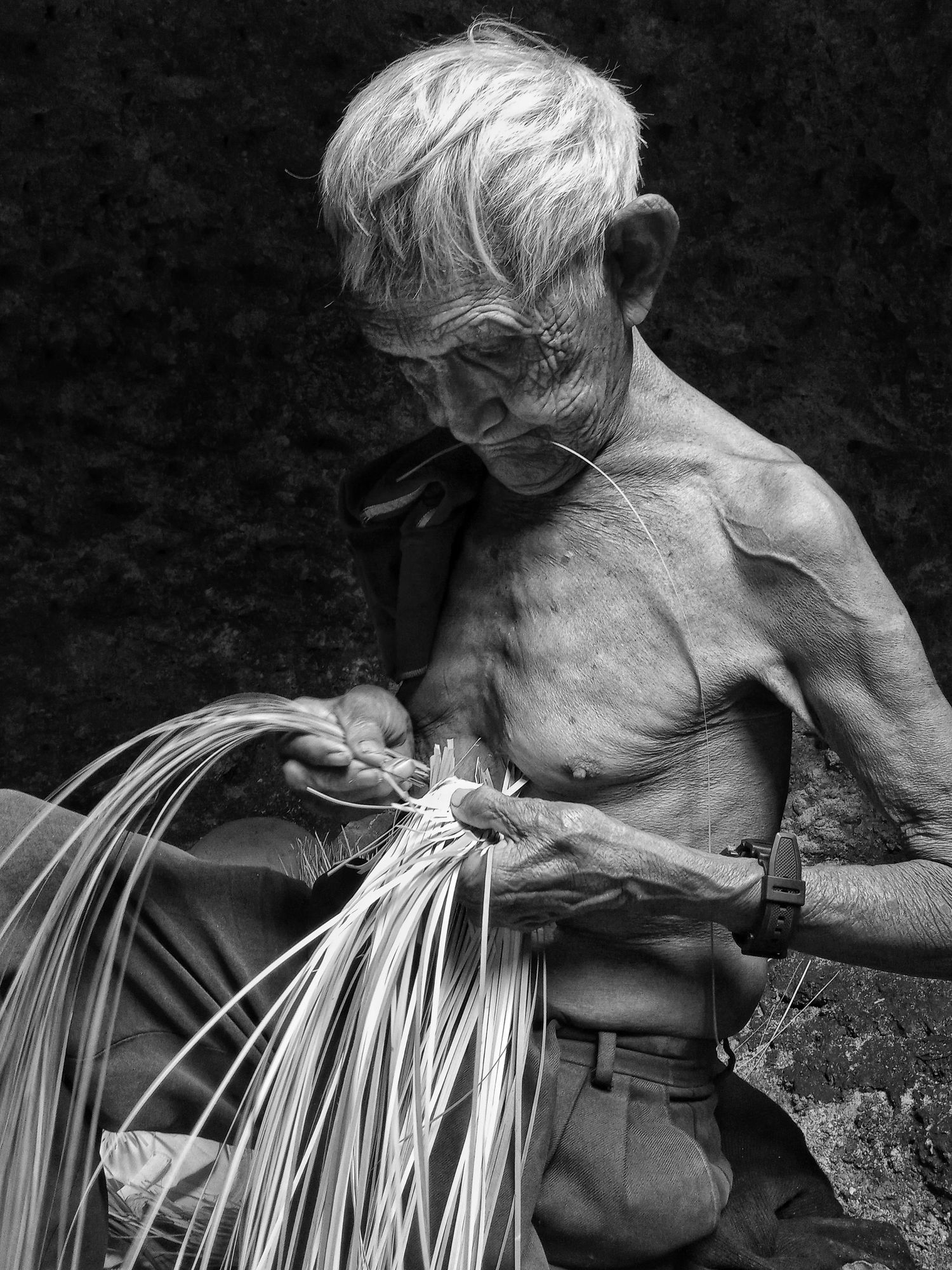 un señor artesano en blanco y negro tejiendo con hojas de palma sobre su cuerpo